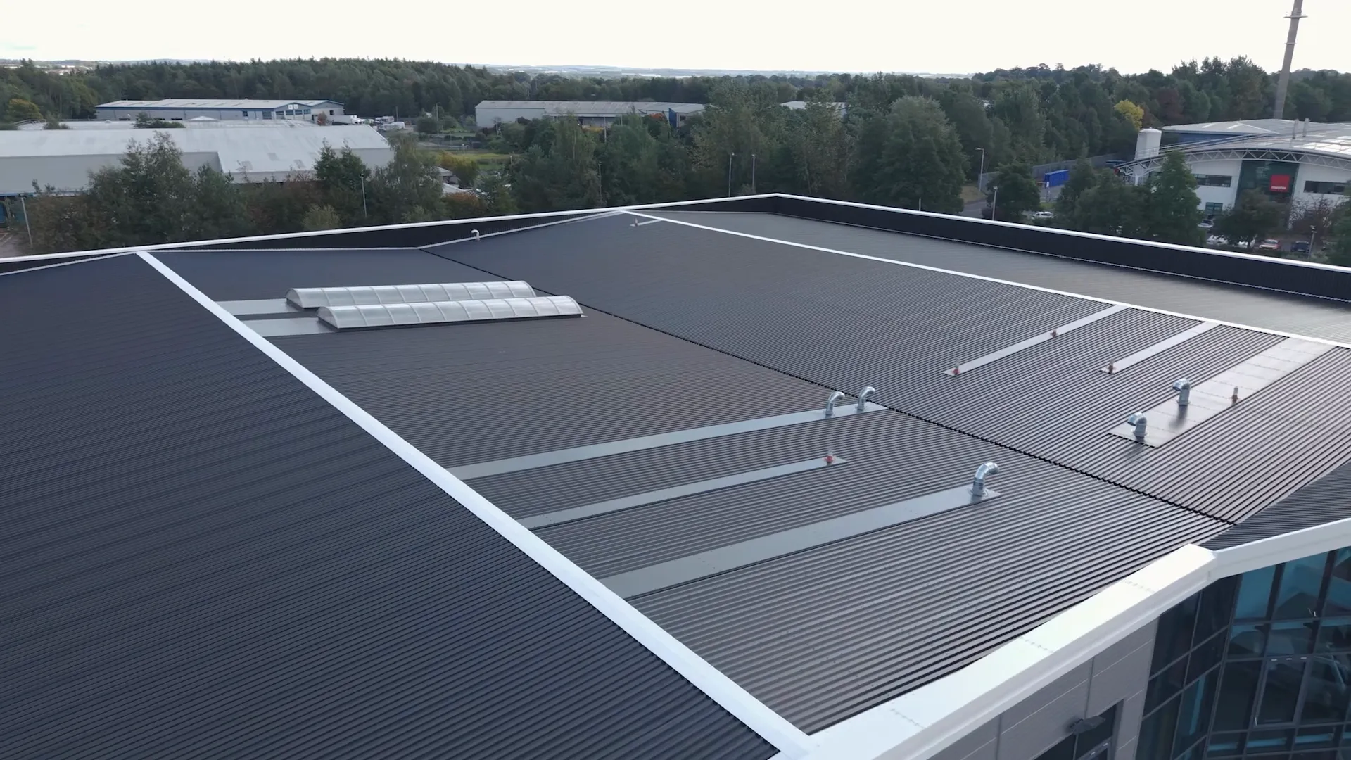 Aerial view across the dark metal roof, curved rooflights and ventilation details at the DFYNE project.