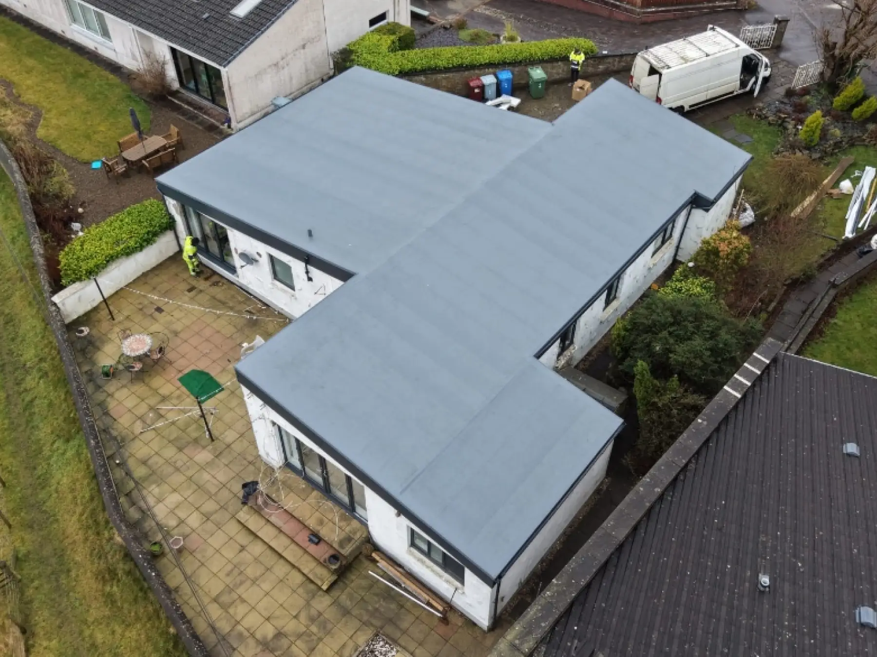 Drone view of a single-storey house in Strathaven with its new grey flat roof and two workers in hi-vis