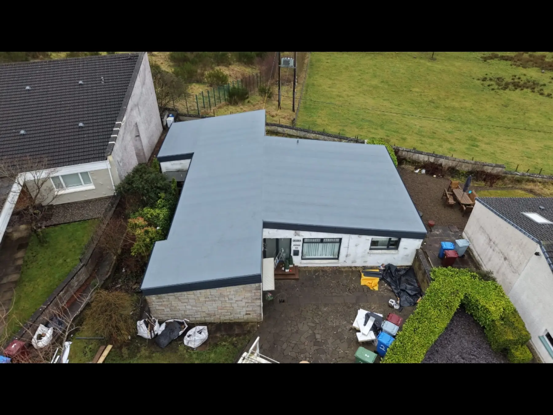 Drone view of the new grey flat roof on a single-storey house in Strathaven, with bulk waste bags in the garden