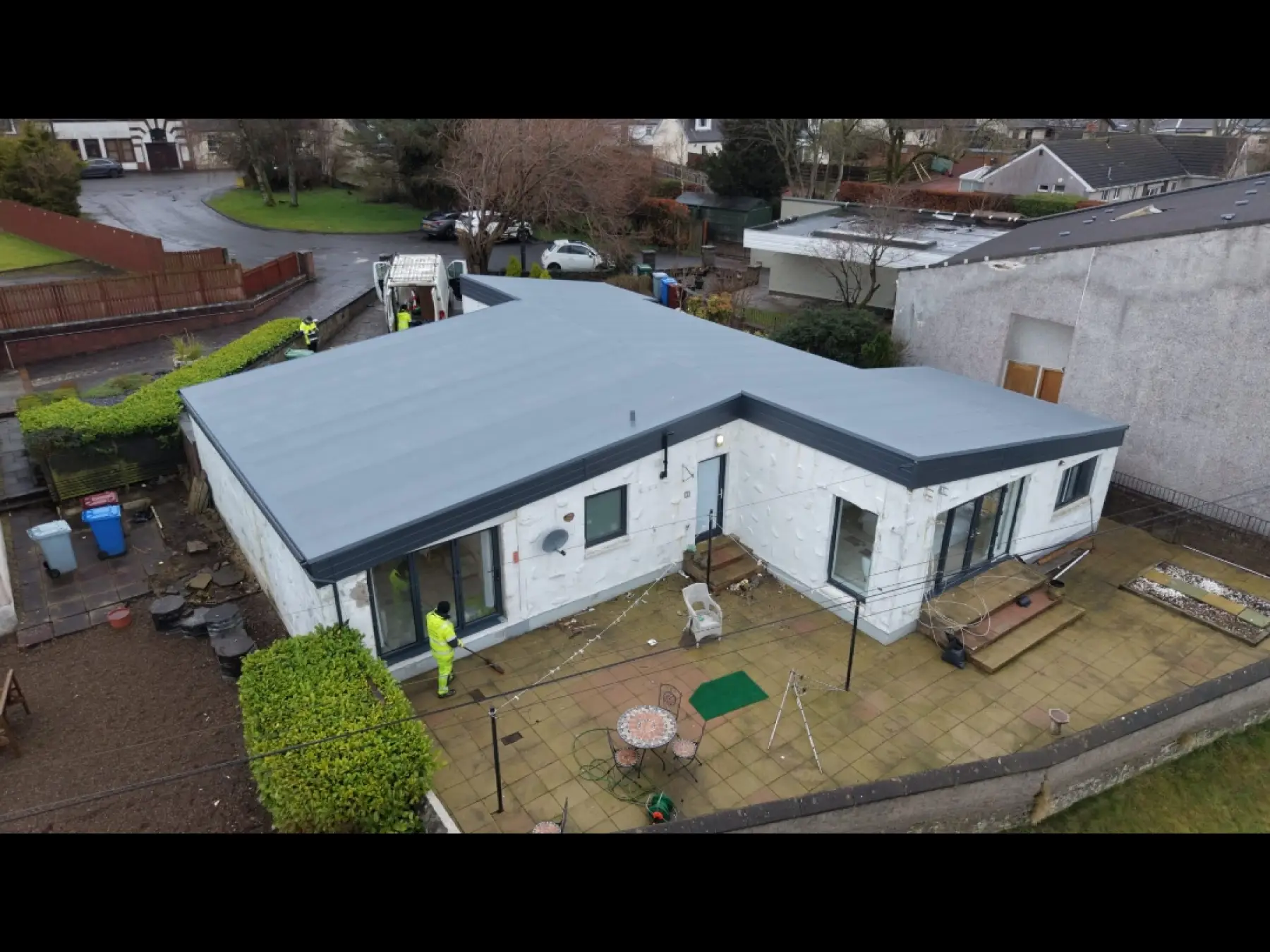 Aerial view of the new grey flat roof and dark fascia in Strathaven as a worker in hi-vis sweeps the patio