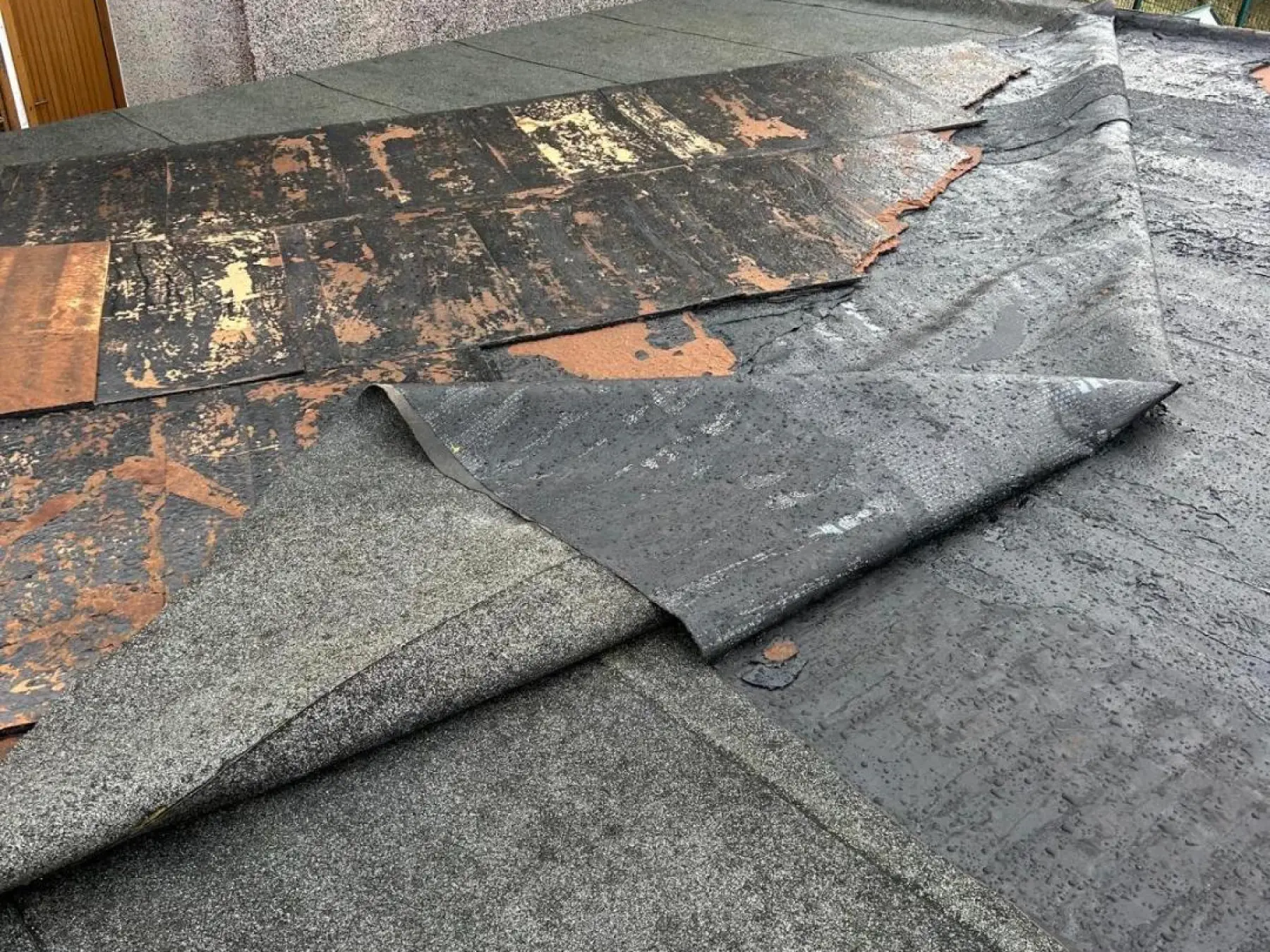 Torn roofing felt peeled back on the Strathaven flat roof, exposing the weathered deck boards beneath