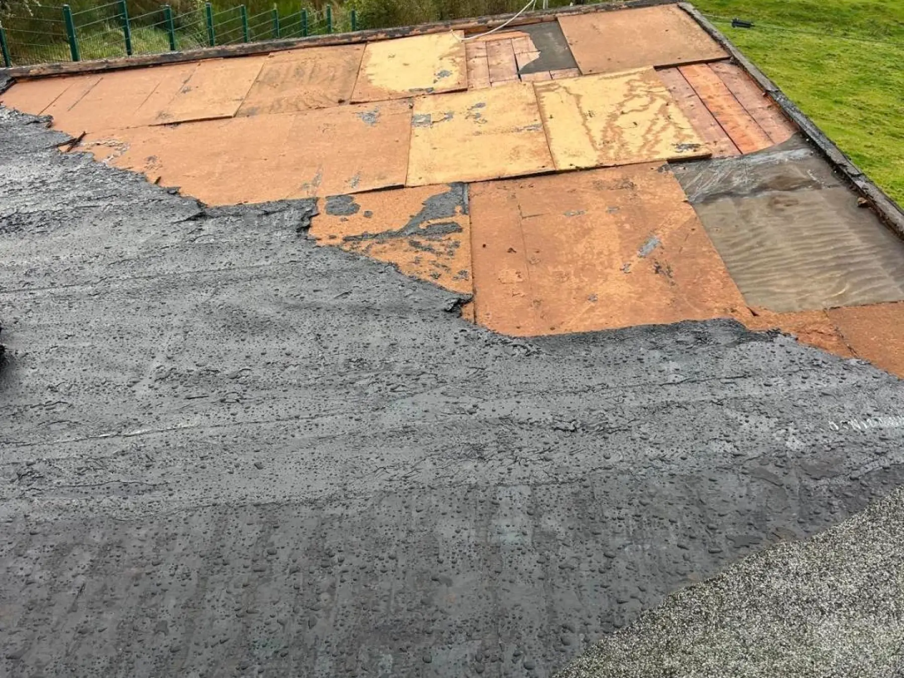 Old roofing felt torn away from the Strathaven flat roof, exposing patched timber deck boards beneath