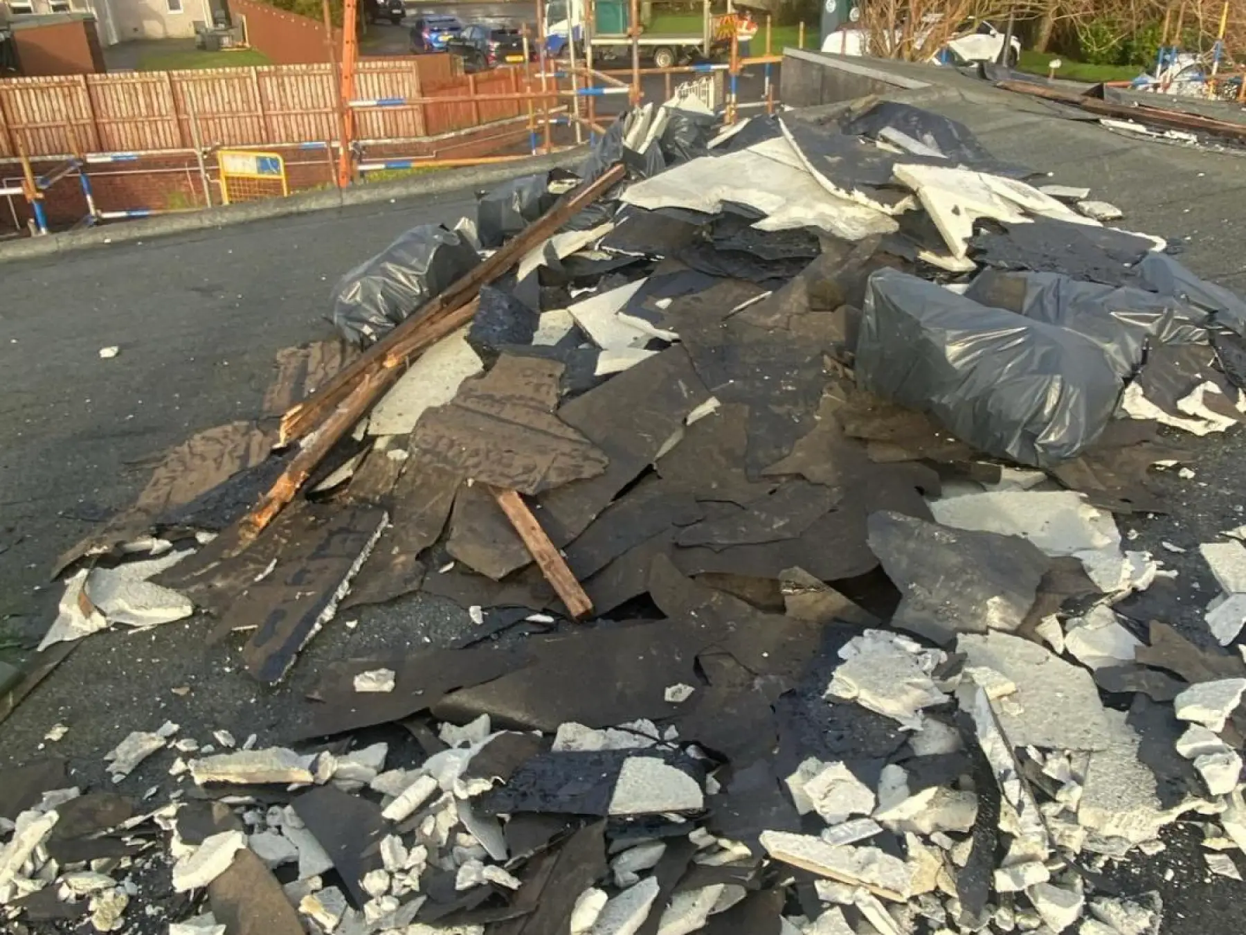 Stripped roofing felt, insulation board and timber piled on a flat roof in Strathaven, with scaffold beyond