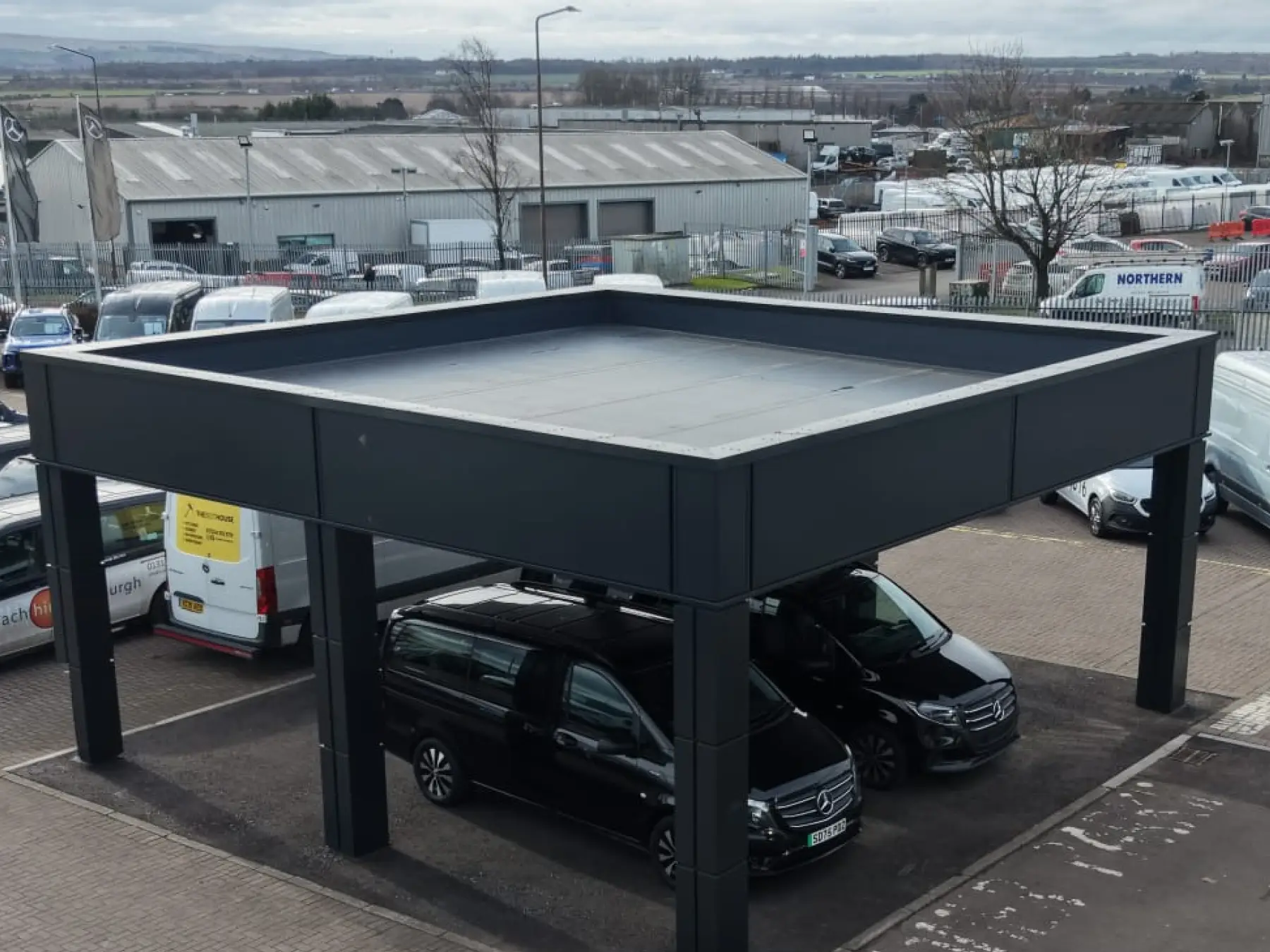Elevated view of a dark grey clad canopy with a flat membrane roof over parked vans at a site in Broxburn