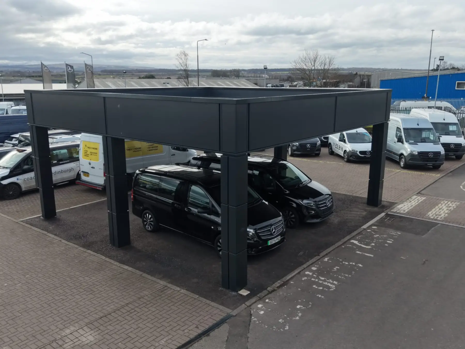 Dark grey clad canopy on four columns sheltering two black vans in a vehicle yard at a site in Broxburn