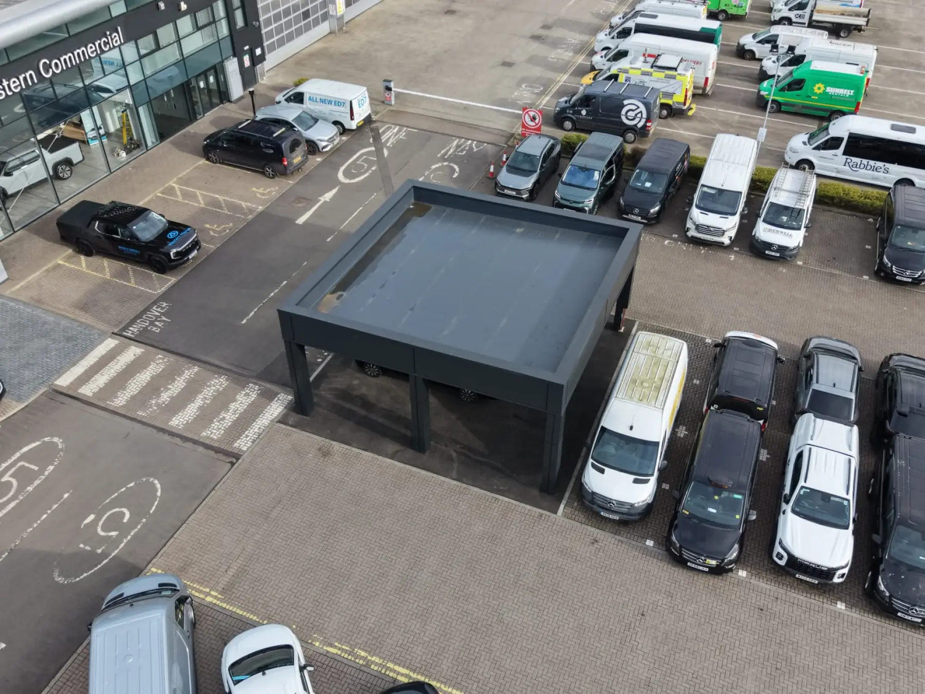 Drone view looking down on the flat-roofed clad canopy beside a showroom and car park at a site in Broxburn
