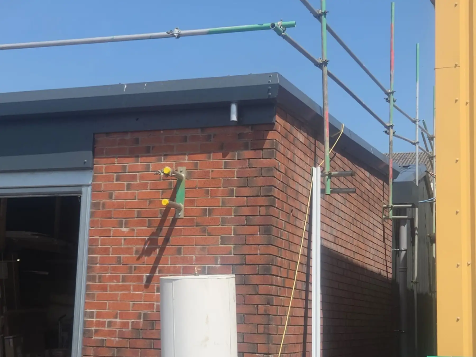 Brick building corner at Gibson & Goold, Ayr, with new dark grey metal roof edge trim and scaffolding alongside
