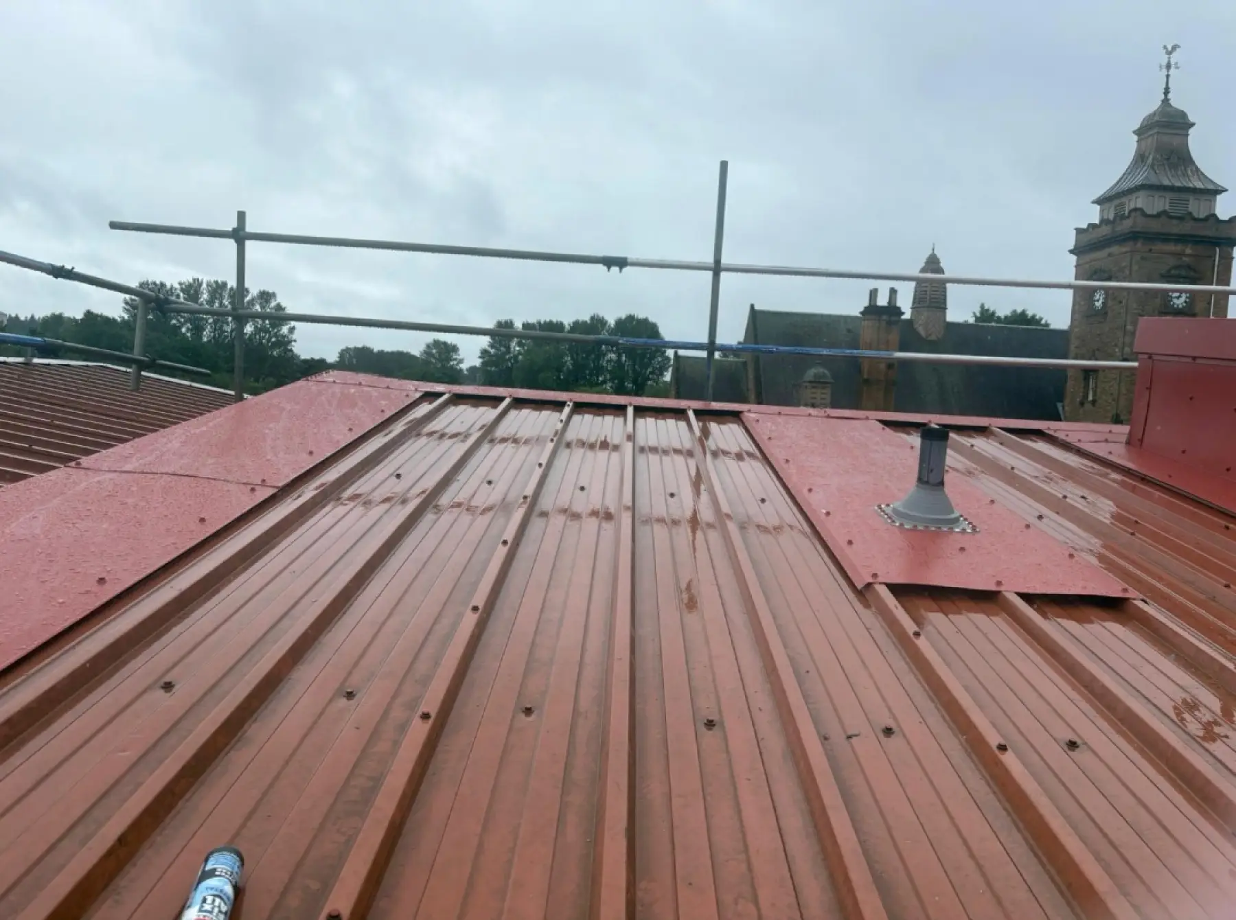 Wet red profiled metal roof for Team Services, Glasgow, with new flashing sheets, a vent pipe and scaffold edge protection