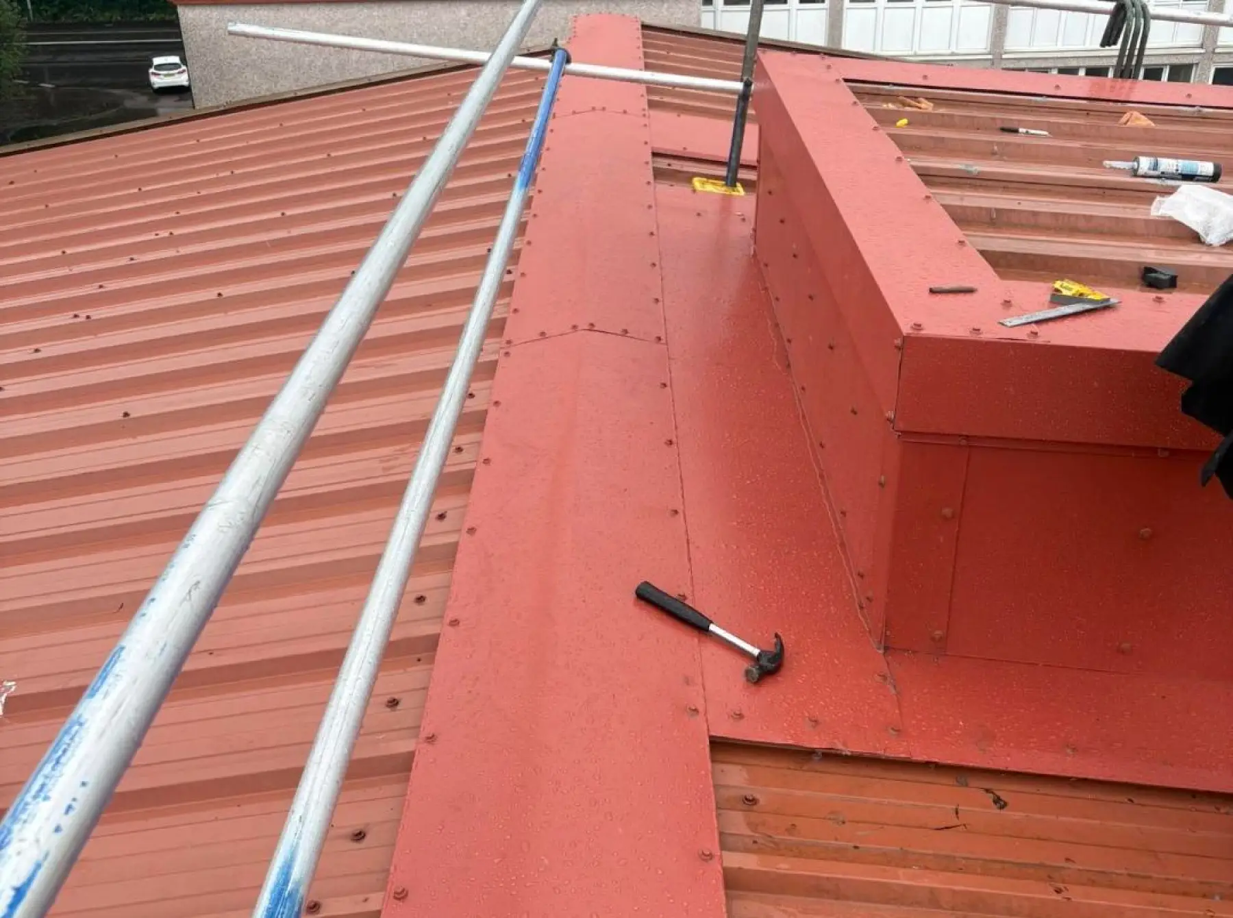 New red flashings fixed around a roof upstand at Team Services, Glasgow, with scaffold tubes and a hammer on the roof