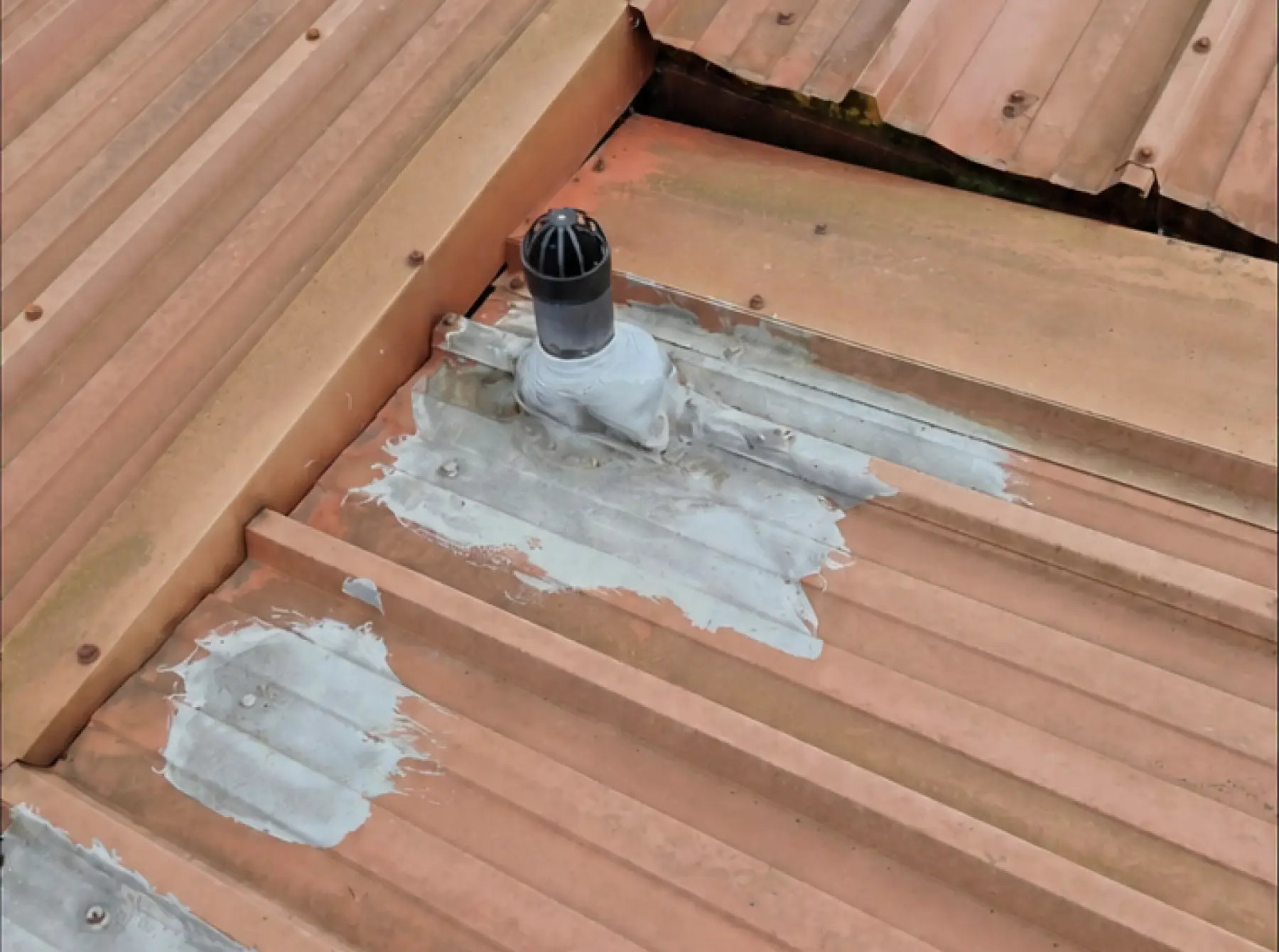 Grey sealant patches around a vent pipe on faded profiled metal roof sheets at Team Services, Glasgow