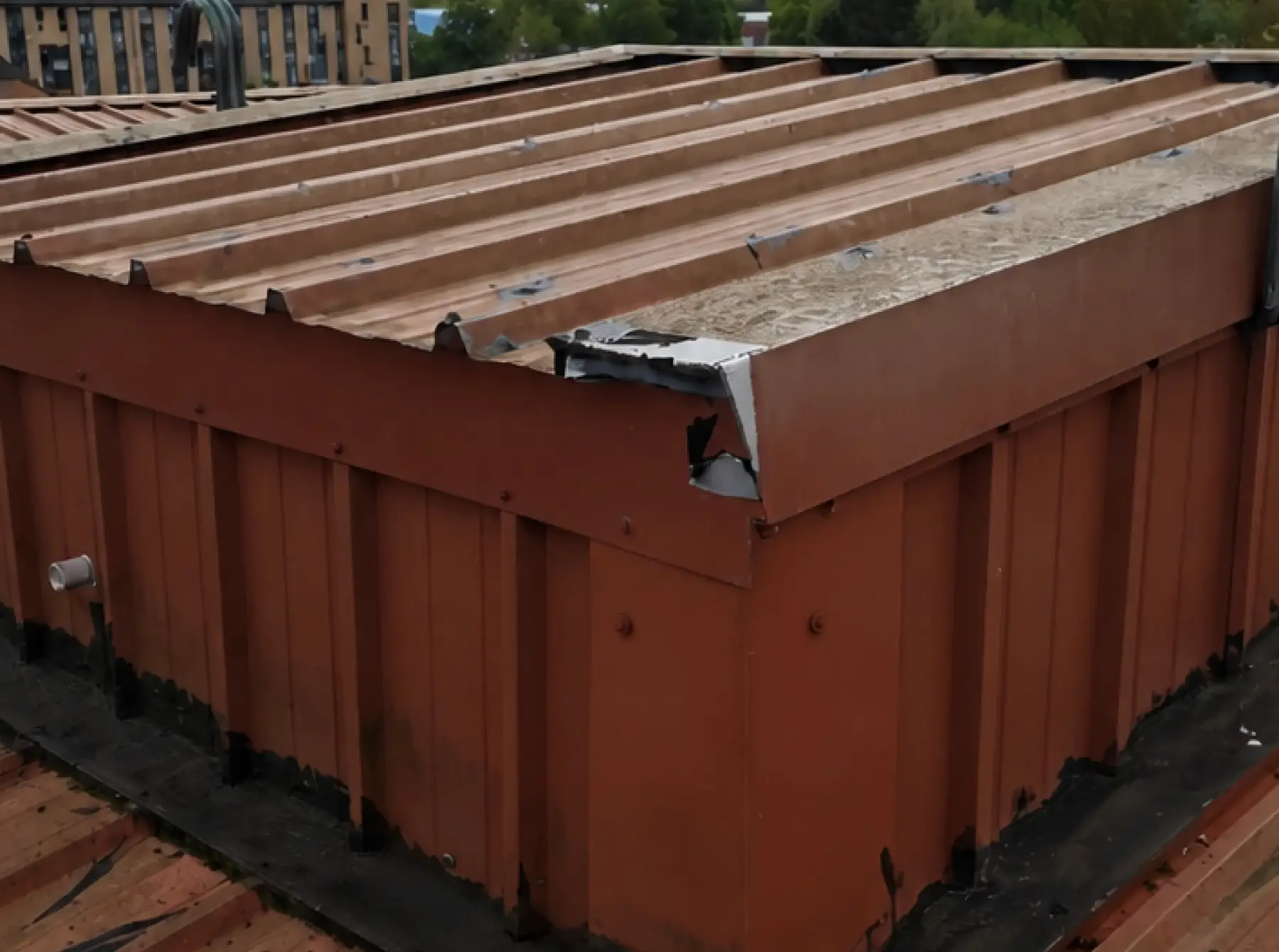 Torn corner flashing on a raised profiled metal roof section at Team Services, Glasgow, with old black sealant at its base