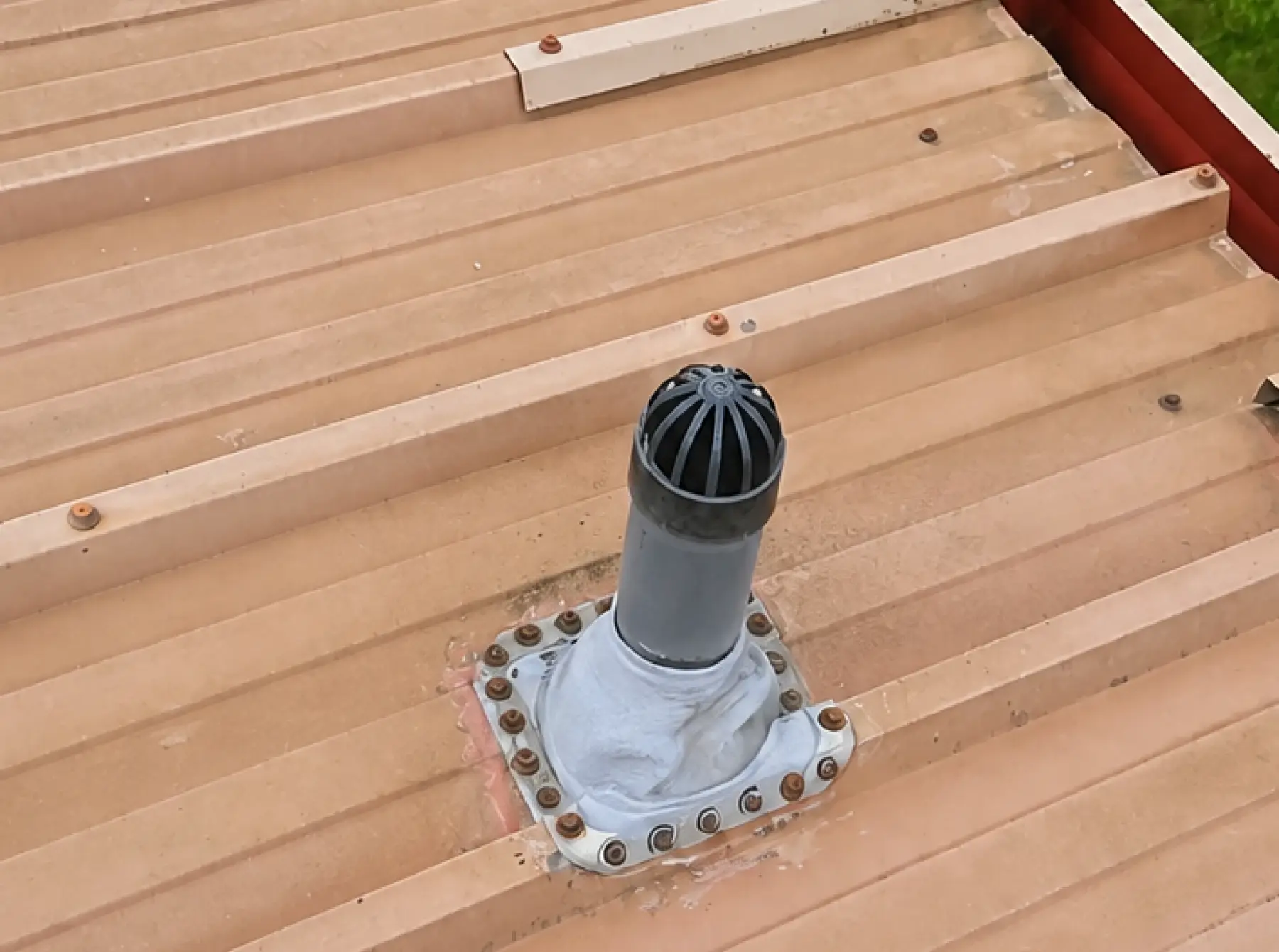 Vent pipe with a bolted and sealed flashing collar on profiled metal roof sheets at Team Services, Glasgow