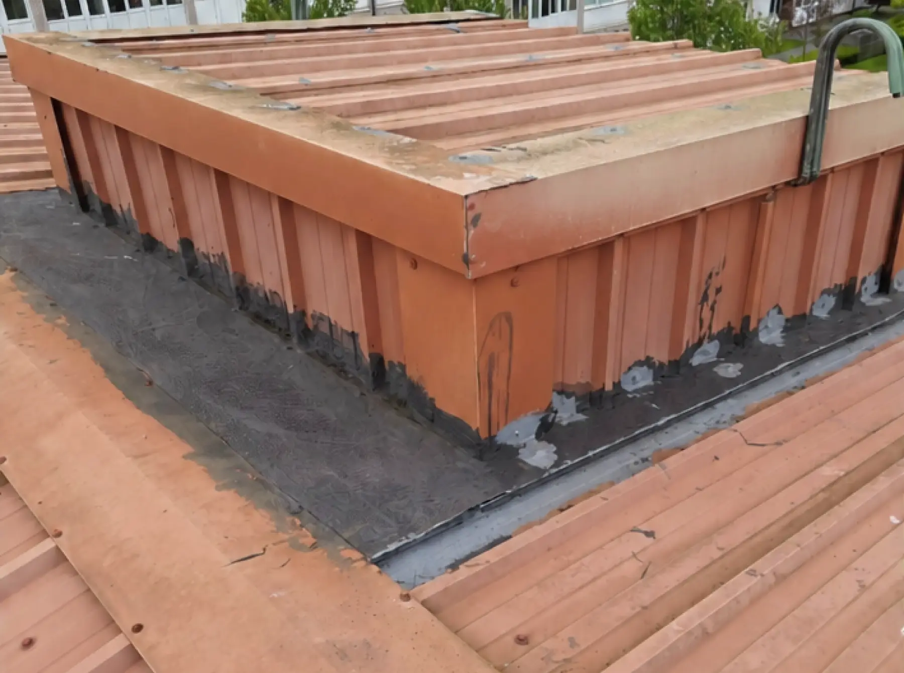 Raised roof section at Team Services, Glasgow, with faded red metal cladding and patched black sealant along its base