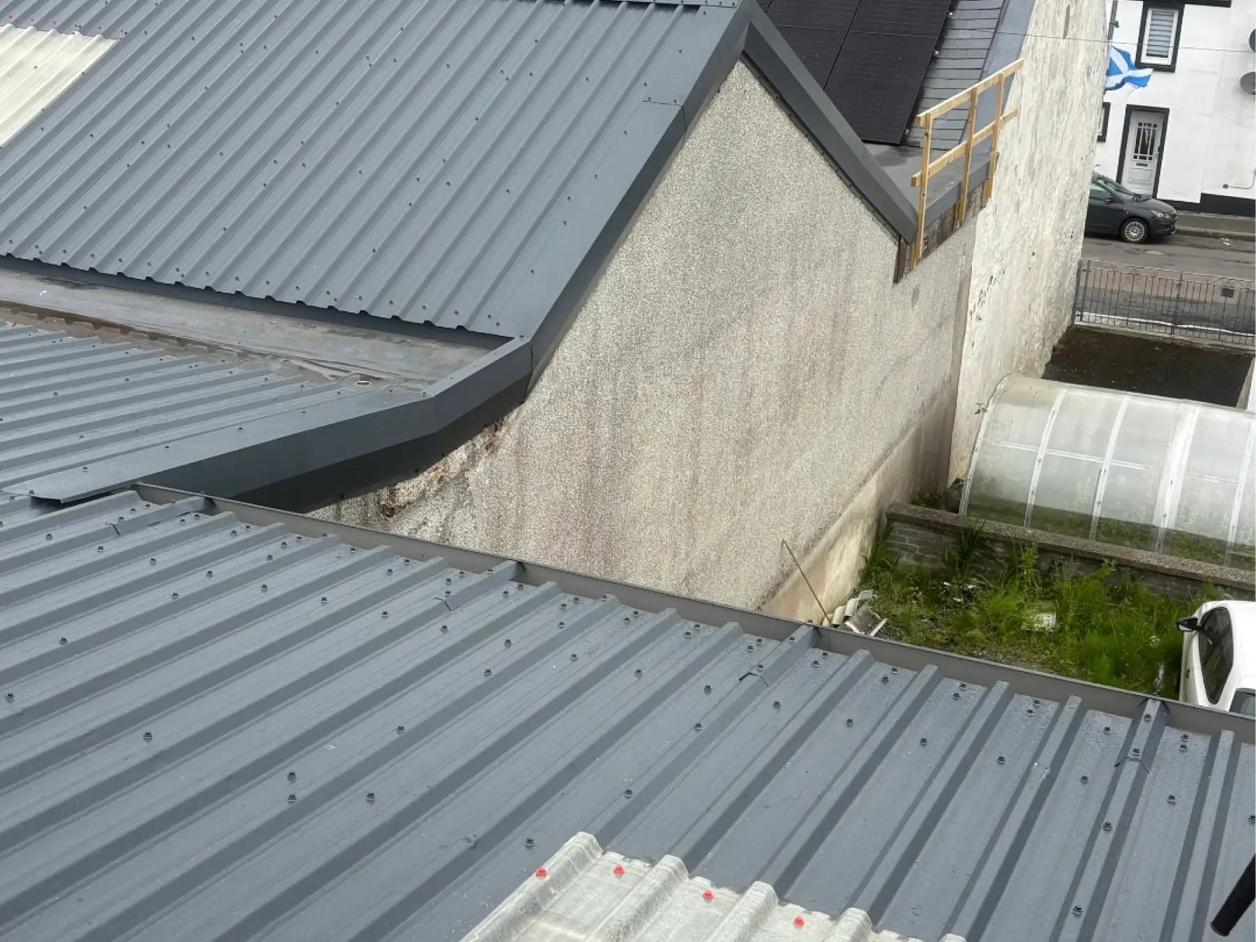 New grey profiled metal sheets, verge flashings and a gutter beside a roughcast gable wall at Bowmore Hall, Islay