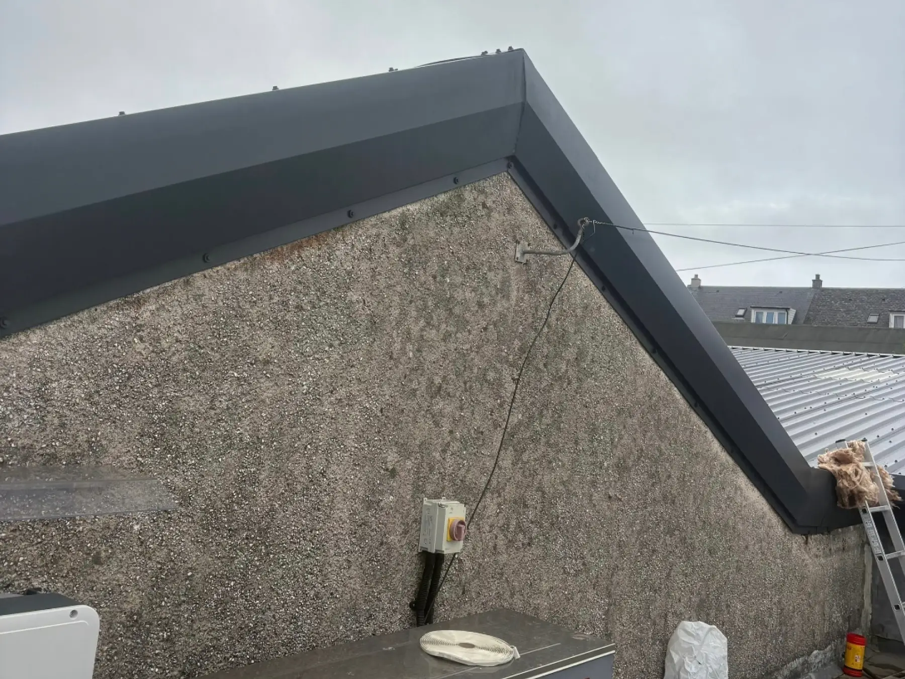 New dark grey metal verge flashings on a pebbledash gable at Bowmore Hall, Islay, with profiled roof sheets beyond