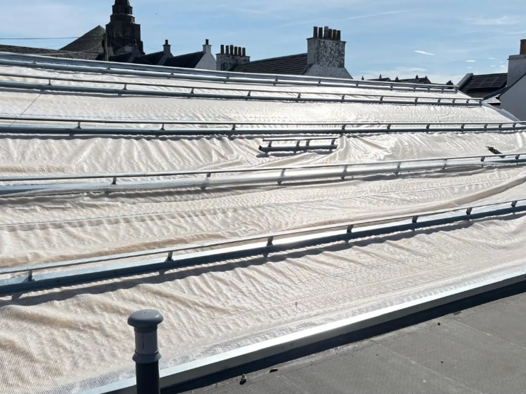White roofing membrane and galvanised spacer rails across the pitched roof at Bowmore Hall, Islay, with chimneys behind