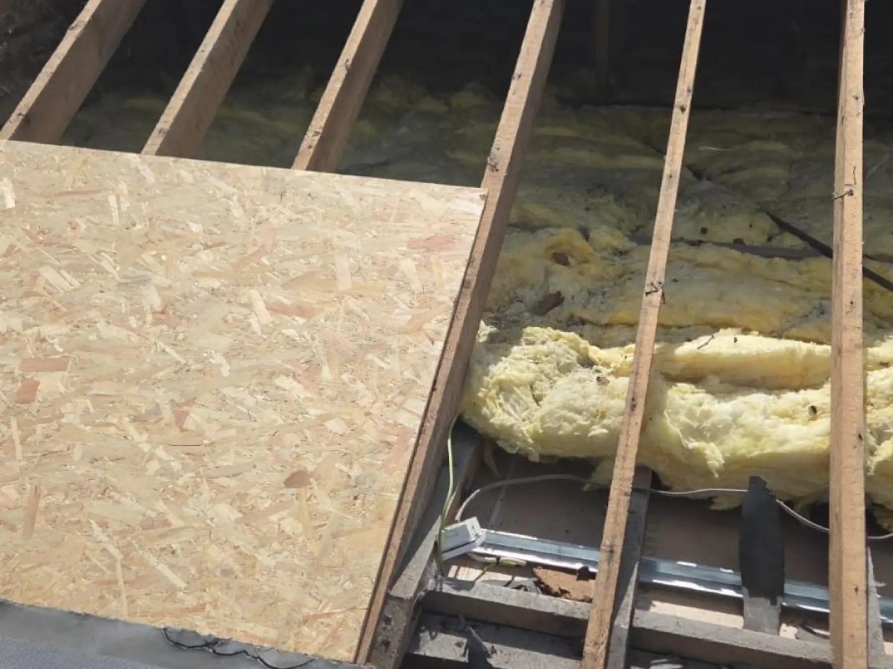 Exposed timber rafters and old yellow insulation, with a new OSB board laid over part of the roof at Bowmore Hall, Islay