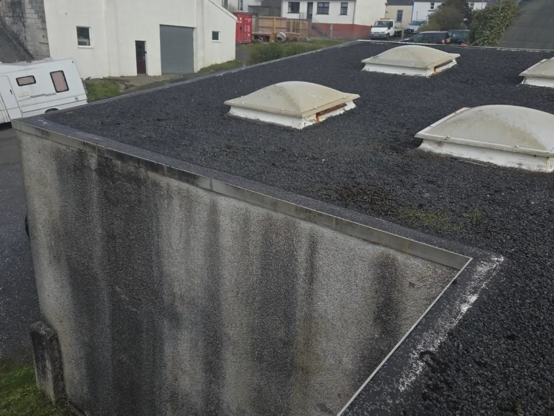 Flat roof with dark stone chippings and dome rooflights at Bowmore Hall, Islay, seen from above the rendered wall edge