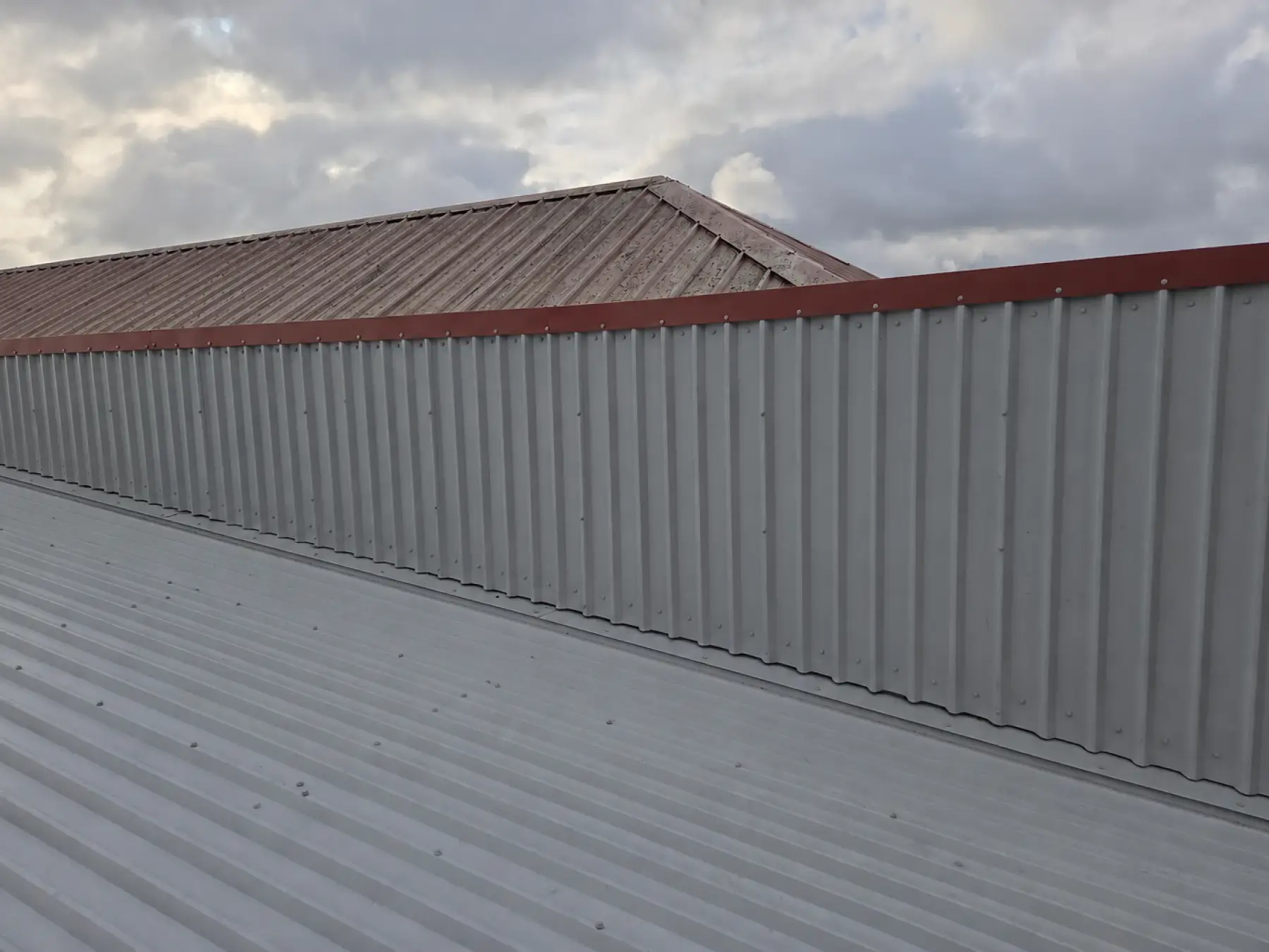 Grey profiled cladding with red capping on a raised wall above the metal roof at Phoenix Medical, East Kilbride
