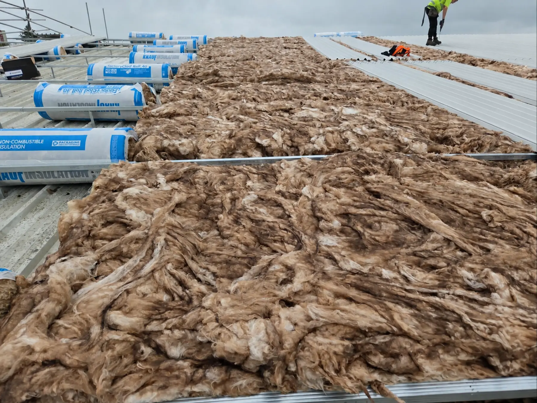 Mineral wool insulation laid between rails on the old roof at Phoenix Medical, East Kilbride, with a roofer beyond