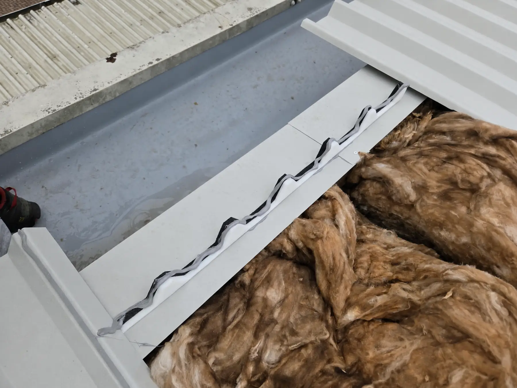 Foam profile fillers on a flashing beside mineral wool and new metal sheets at Phoenix Medical, East Kilbride