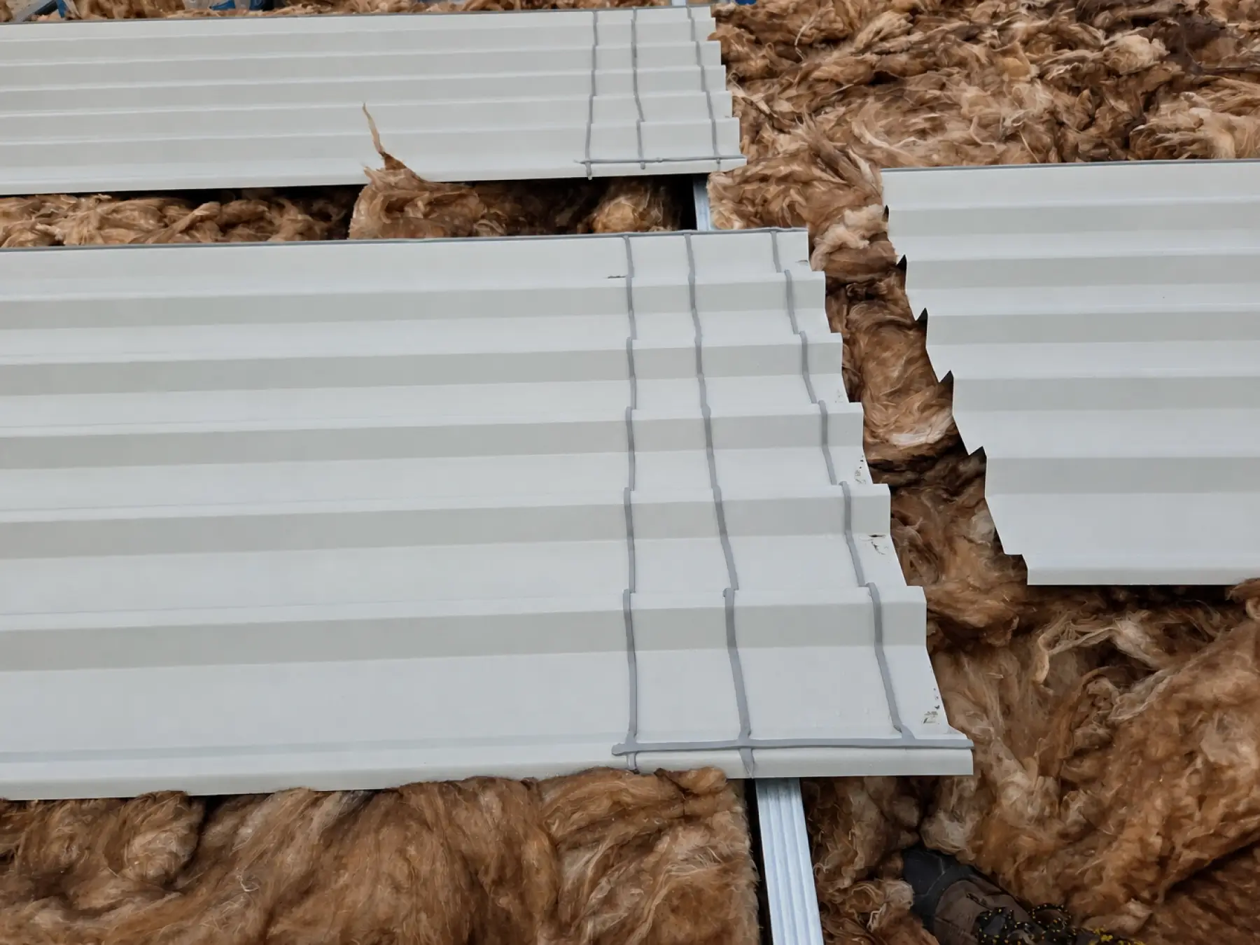 New grey profiled metal sheets with sealant strips laid over mineral wool insulation at Phoenix Medical, East Kilbride