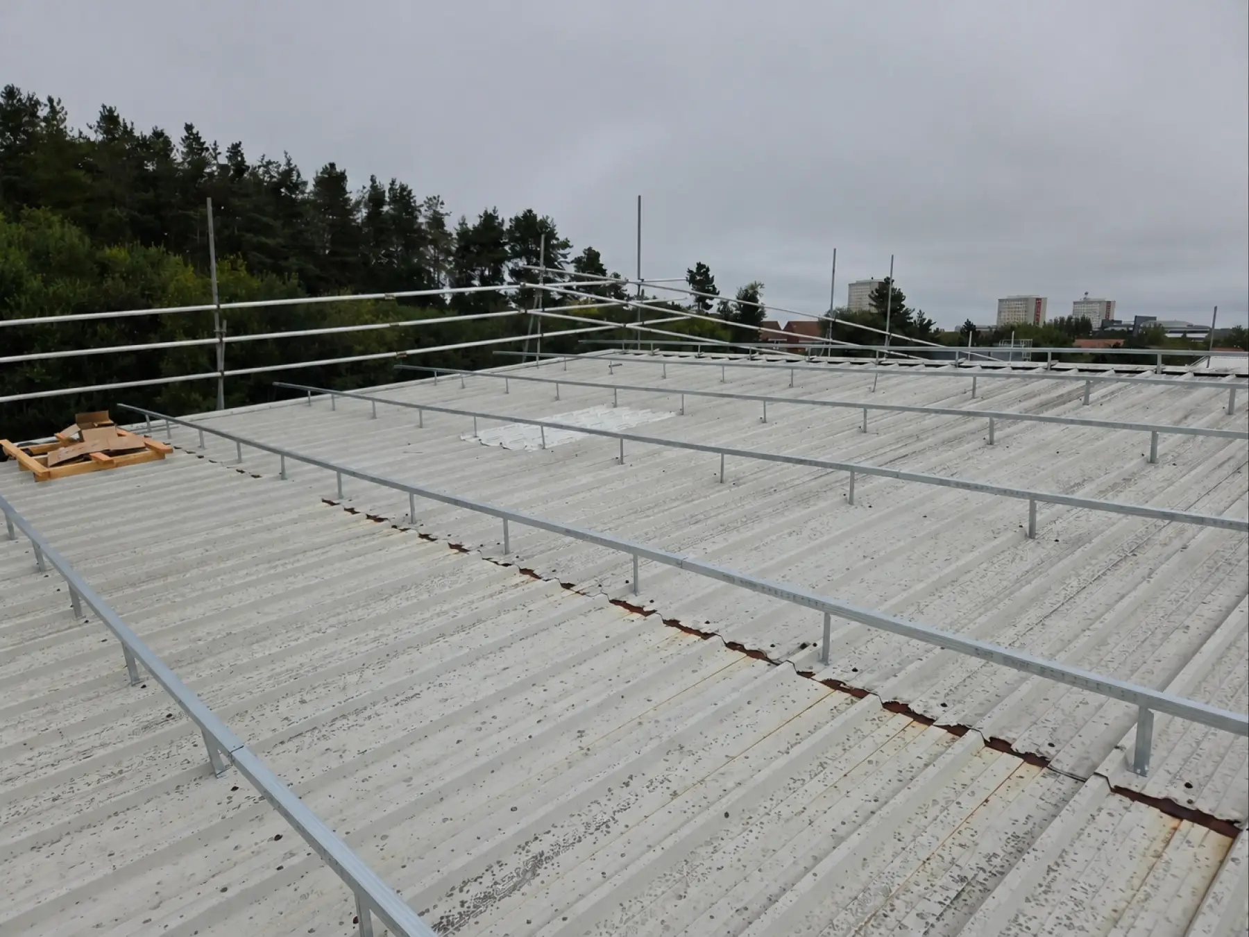 Spacer rails over the existing metal roof with rusted sheet laps and edge protection at Phoenix Medical, East Kilbride