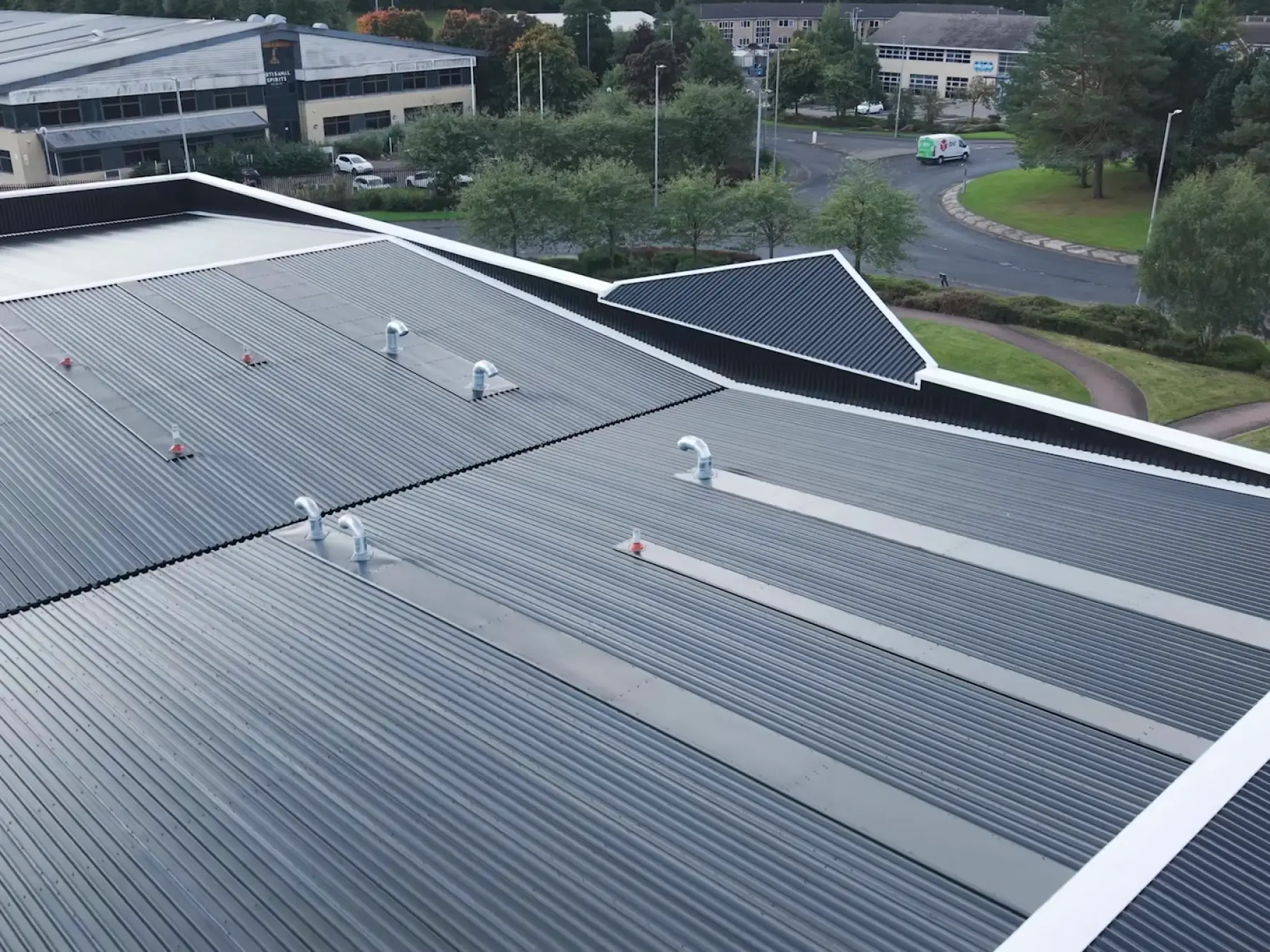 Aerial view of a new dark grey profiled metal roof with vent pipes and white edge trims on an industrial unit