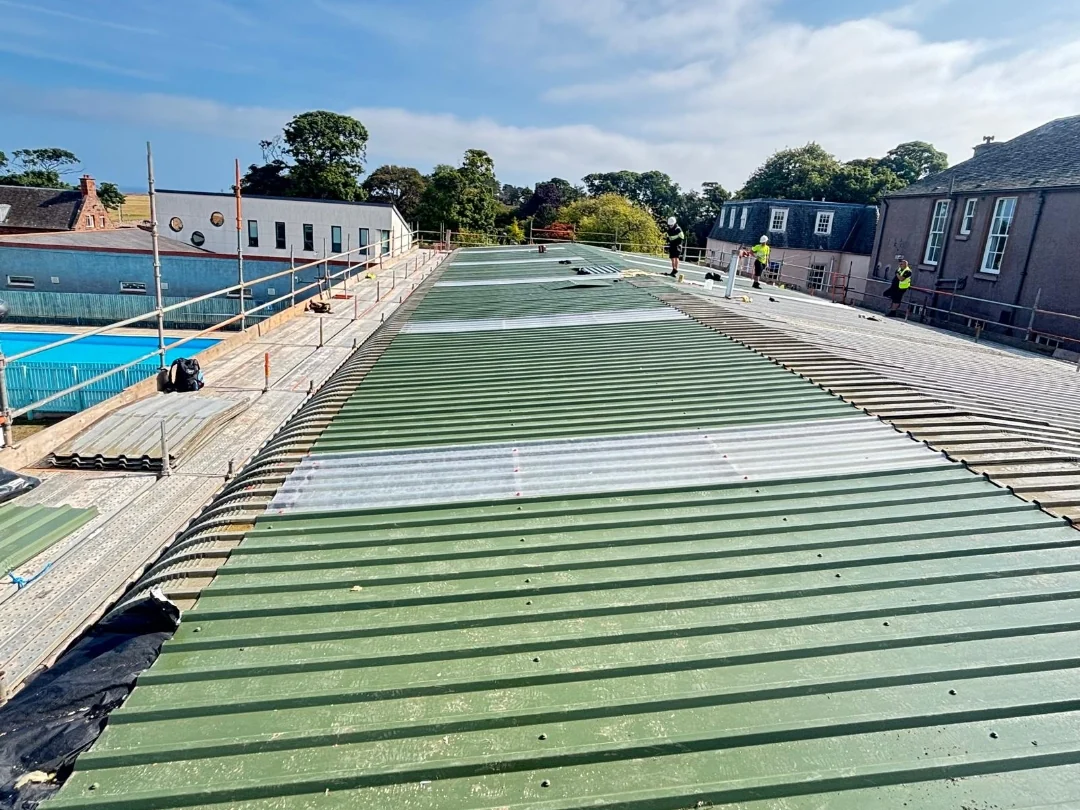 Green profiled metal roofing and rooflights during installation at a school.
