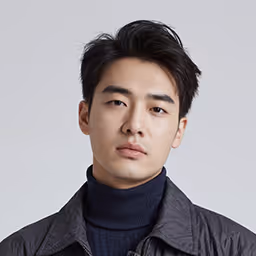 Portrait of a young man with short black hair wearing a black turtleneck and a dark jacket against a light gray background.
