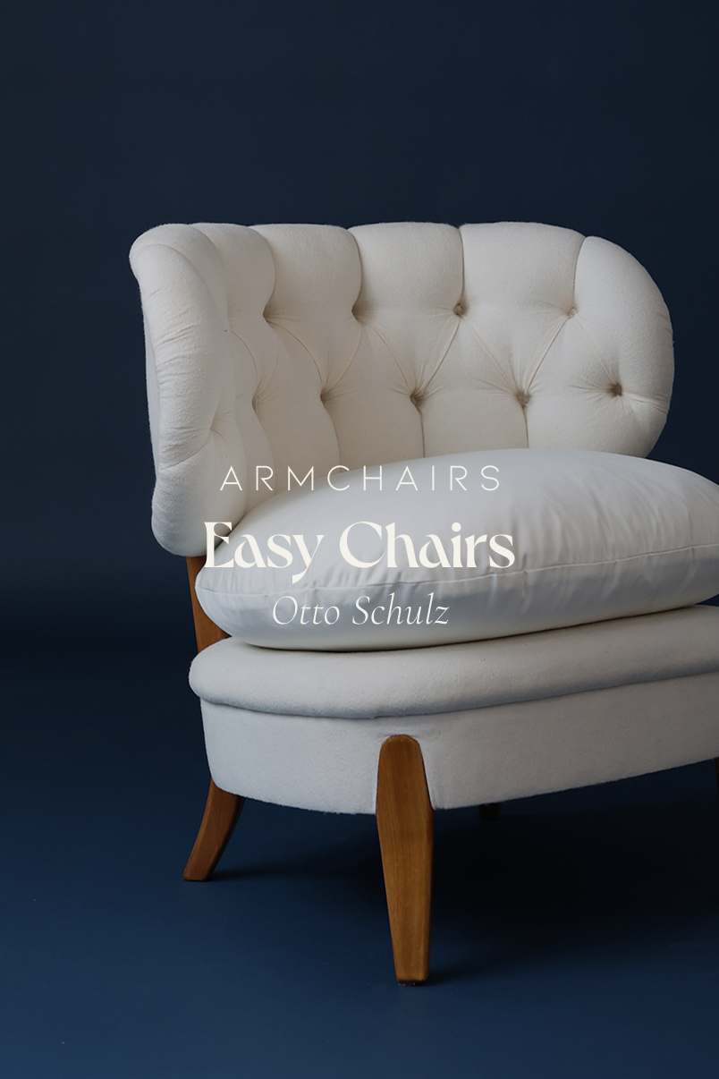 A straight-on product shot of a pair of elegant, front-facing Otto Schulz upholstered easy chairs with white fabric on a deep blue background.