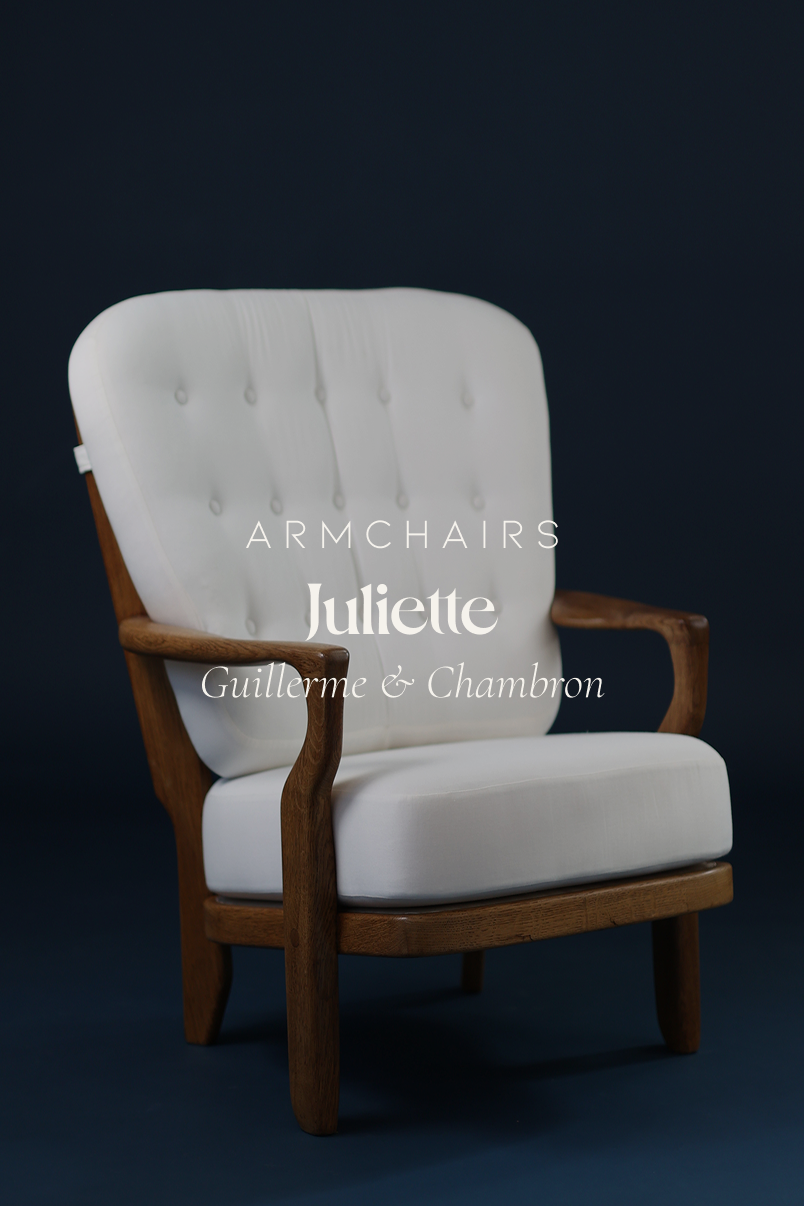 Juliette armchair by Guillerme et Chambron, front view showing the light wood frame with armrests, the high backrest with spindle structure, and the white upholstered seat against a dark blue background.