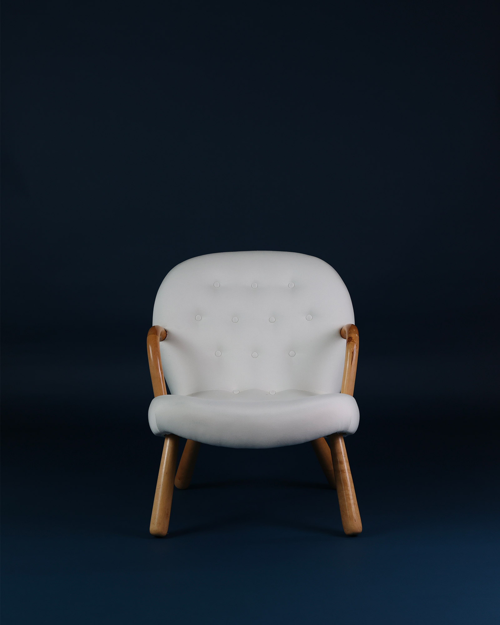 Front view of the mid-century modern Clam chair by Arnold Madsen in soft white fabric with wooden legs.