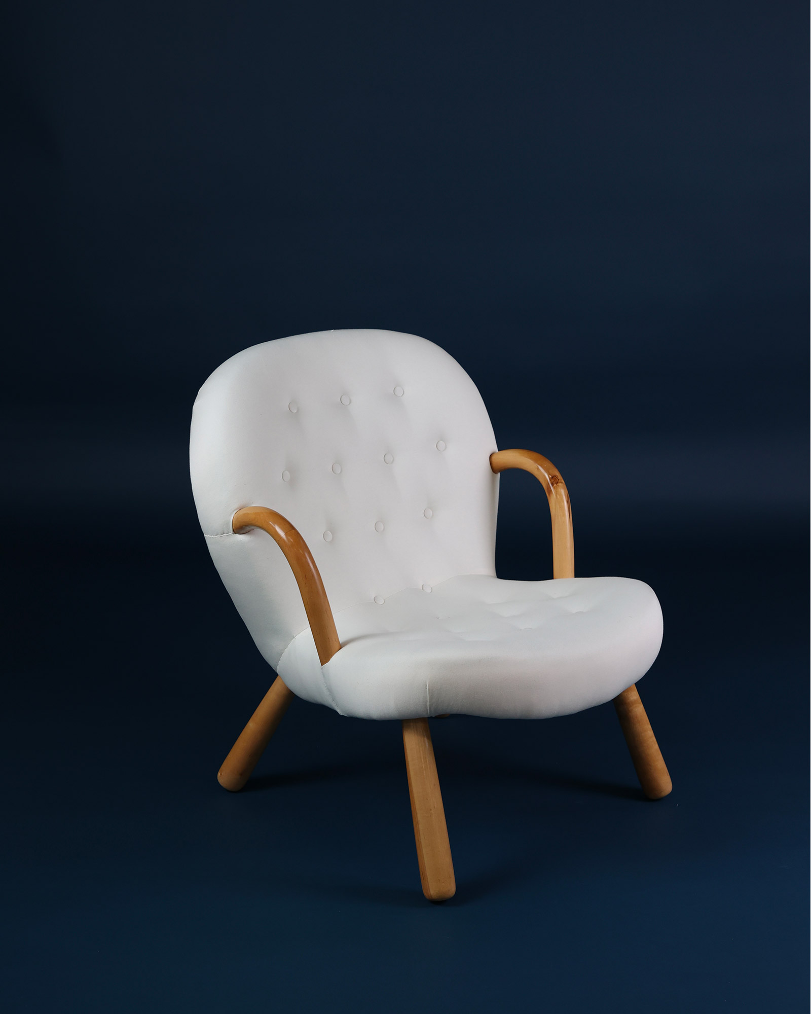 Three-quarter angle view of an Arnold Madsen Clam armchair featuring plush white upholstery and solid wood legs.