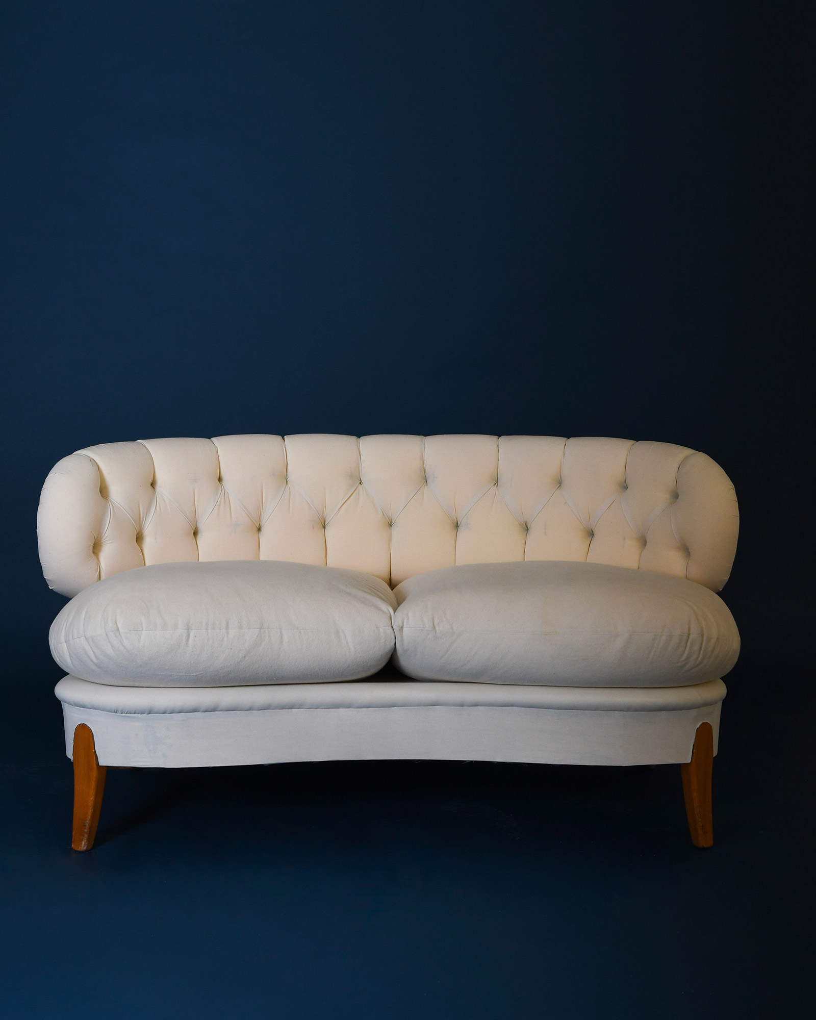 A full front view of the cream-colored, upholstered Boet sofa by Otto Schulz, featuring tapered wooden legs and a distinctive tufted backrest.
