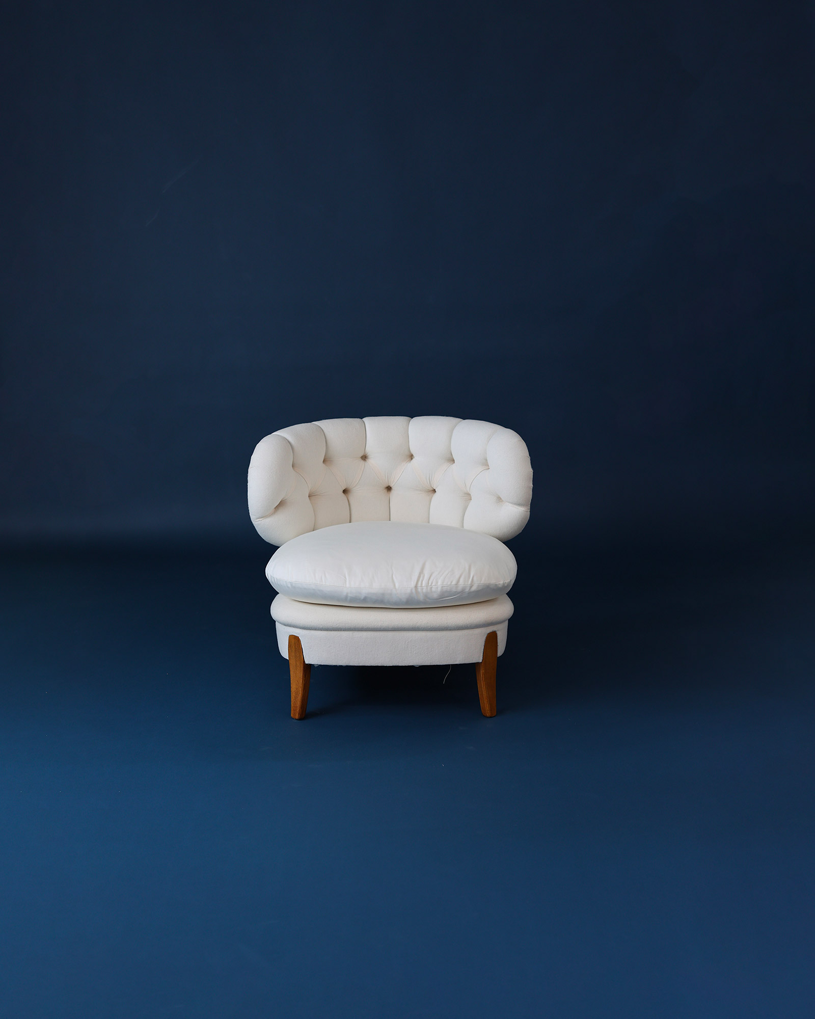 A straight-on product shot of a pair of elegant, front-facing Otto Schulz upholstered easy chairs with white fabric on a deep blue background.