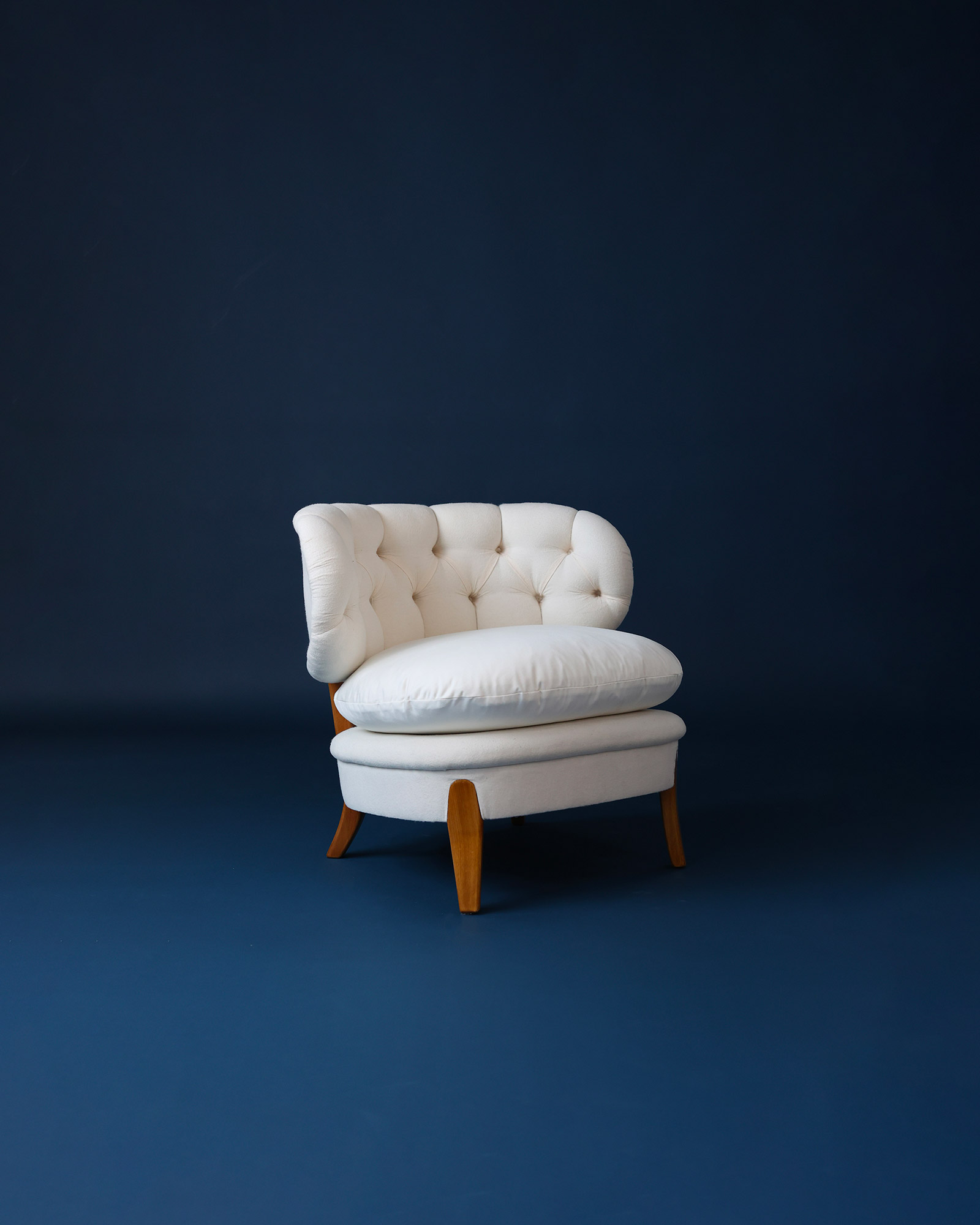 Angled three-quarter perspective product photograph of two classic white Otto Schulz easy chairs against a dark blue studio backdrop.
