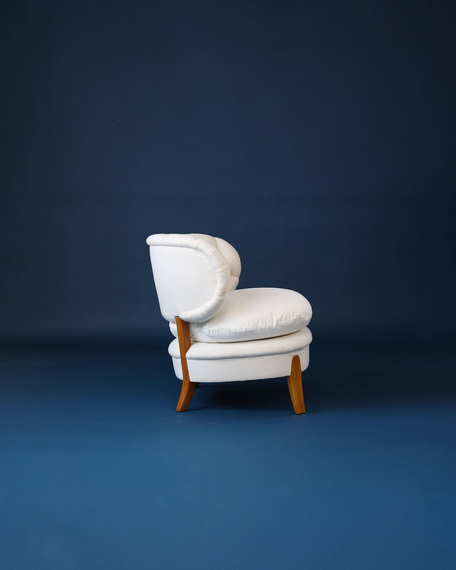 A detailed product profile view of a single vintage white Otto Schulz upholstered easy chair, highlighting its elegant curved form against a dark blue background.