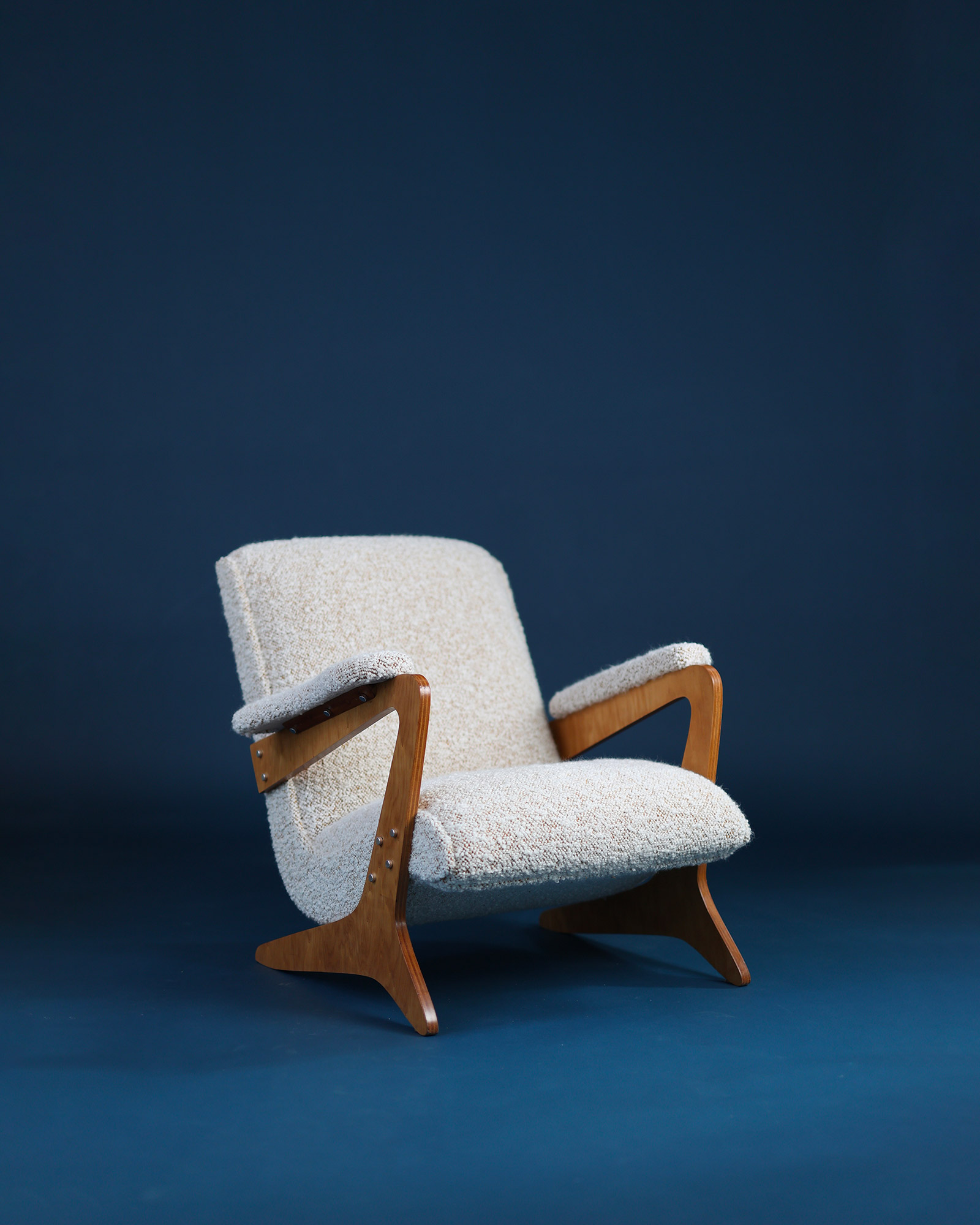 Zeca armchair by José Zanine Caldas - three-quarter front view featuring sculpted wooden armrests and white upholstery on a blue background
