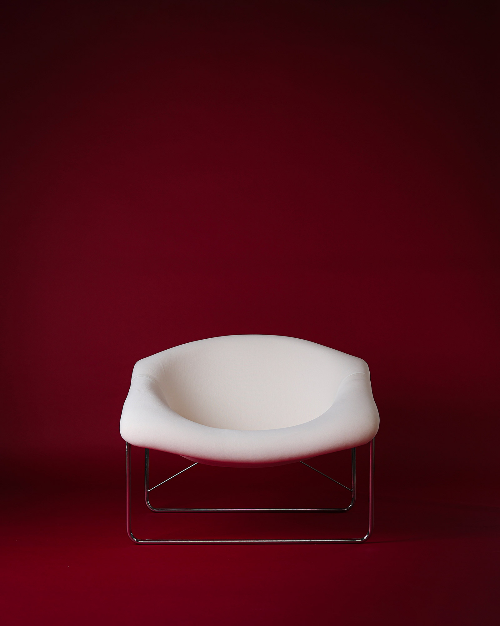 Cubique armchair by Olivier Mourgue - full front view with white seat shell and tubular metal frame on a red background