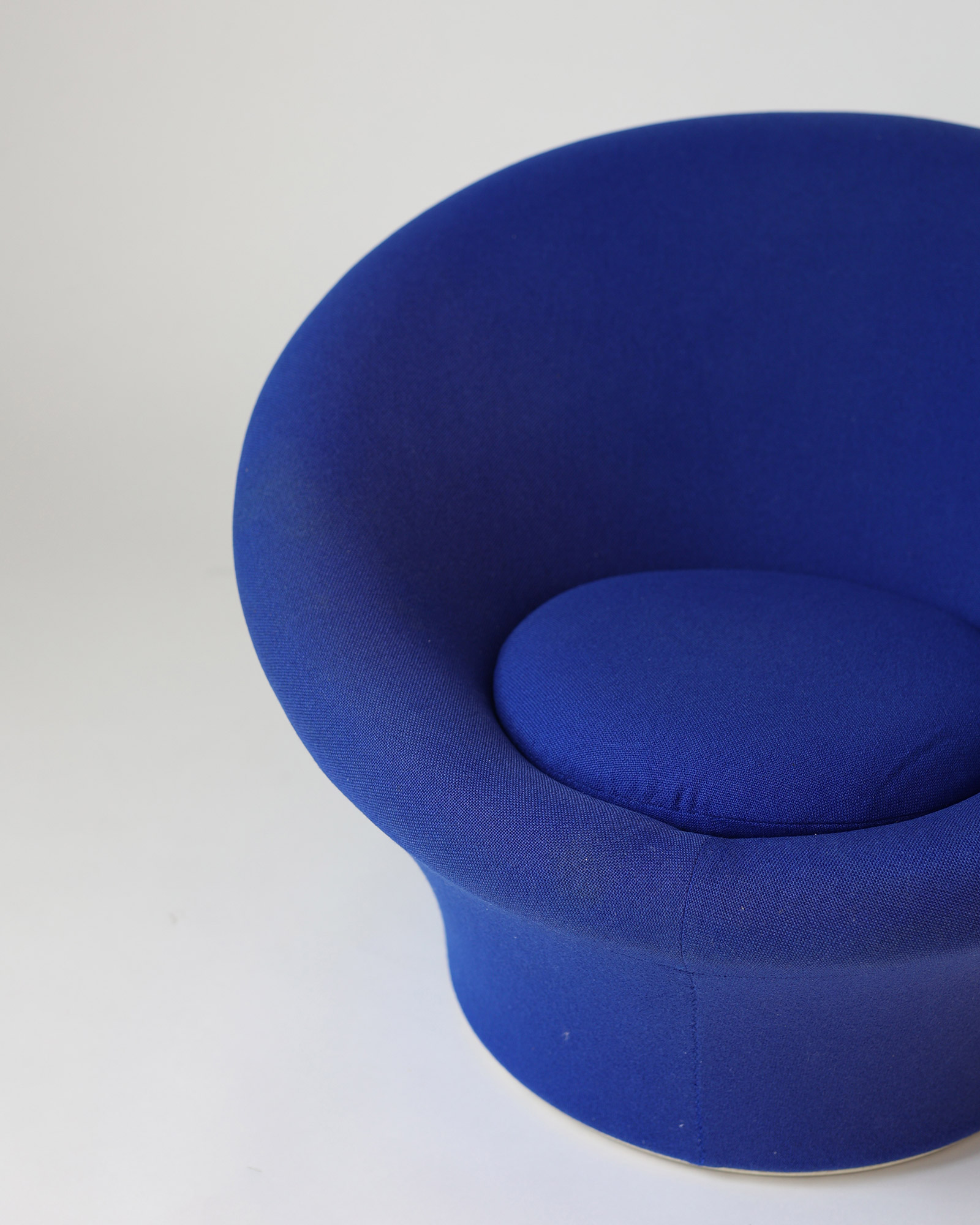A low-angle close-up view focusing on the deep seat and the continuous organic curve of a dark blue upholstered Pierre Paulin Mushroom lounge chair.