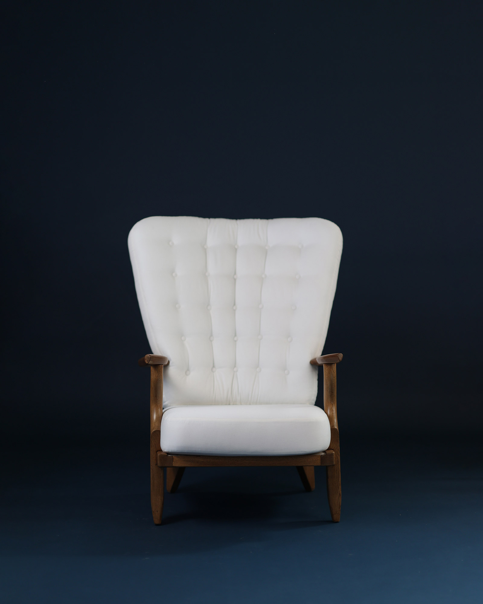 Grand Repos armchair by Guillerme et Chambron - full front view with white fabric upholstery and solid oak frame on a dark blue background