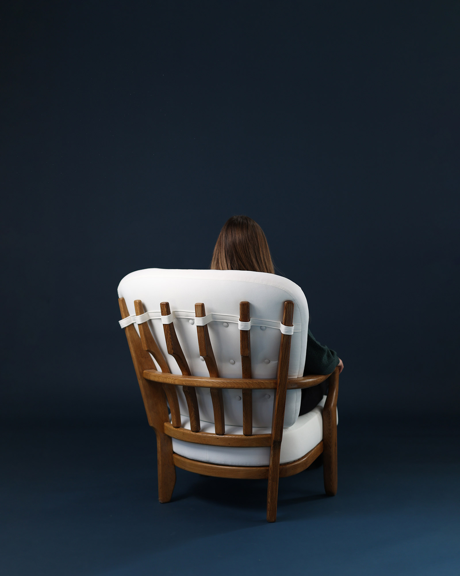 A three-quarter view from the rear-right of the Juliette armchair by Guillerme et Chambron, emphasizing the intricate wooden spindle cage backrest structure and the side of the white seat.