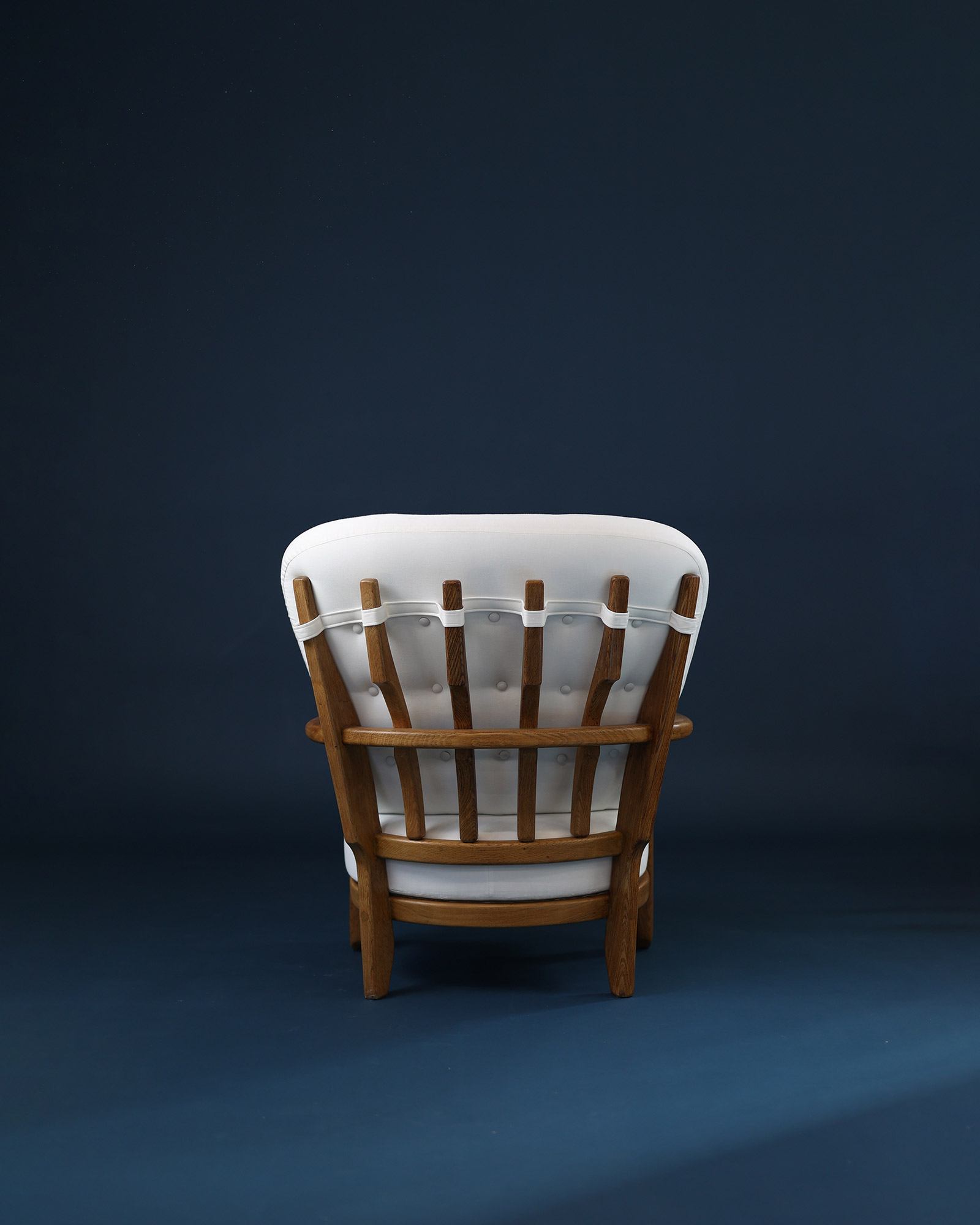 A three-quarter view from the rear-left of the Juliette armchair by Guillerme et Chambron, showcasing the detailed wooden spindle backrest grid and the rear frame structure.