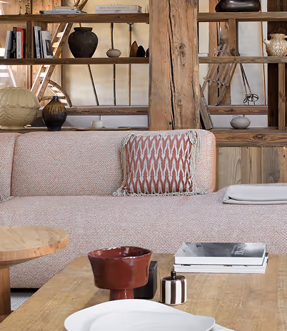 Canapé beige avec coussin rouge, table basse en bois avec objets décoratifs et étagères en bois derrière, La Ferme des Drus, Chamonix-Mont-Blanc, France.