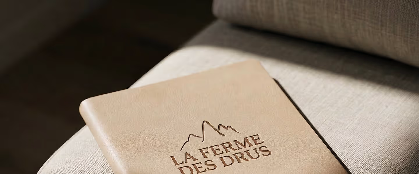Un carnet beige avec le logo montagne et le texte La Ferme des Drus gravé dessus, La Ferme des Drus, Chamonix-Mont-Blanc, France.
