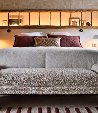 Lit double avec coussins rouge et beige et un banc en tissu beige au pied, miroir et étagère en bois au mur, La Ferme des Drus, Chamonix-Mont-Blanc, France.