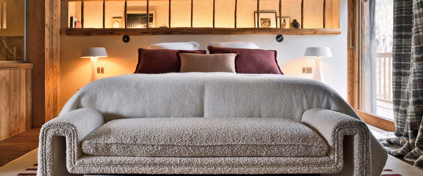 Chambre avec lit king-size, coussins bordeaux, banc en tissu beige et lampe sur chaque côté, La Ferme des Drus, Chamonix-Mont-Blanc, France.