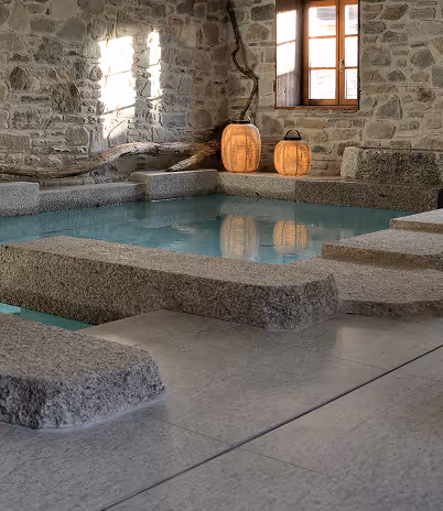 Piscine intérieure en pierre avec lumière naturelle et deux lanternes en bois près d'une fenêtre, La Ferme des Drus, Chamonix-Mont-Blanc, France.