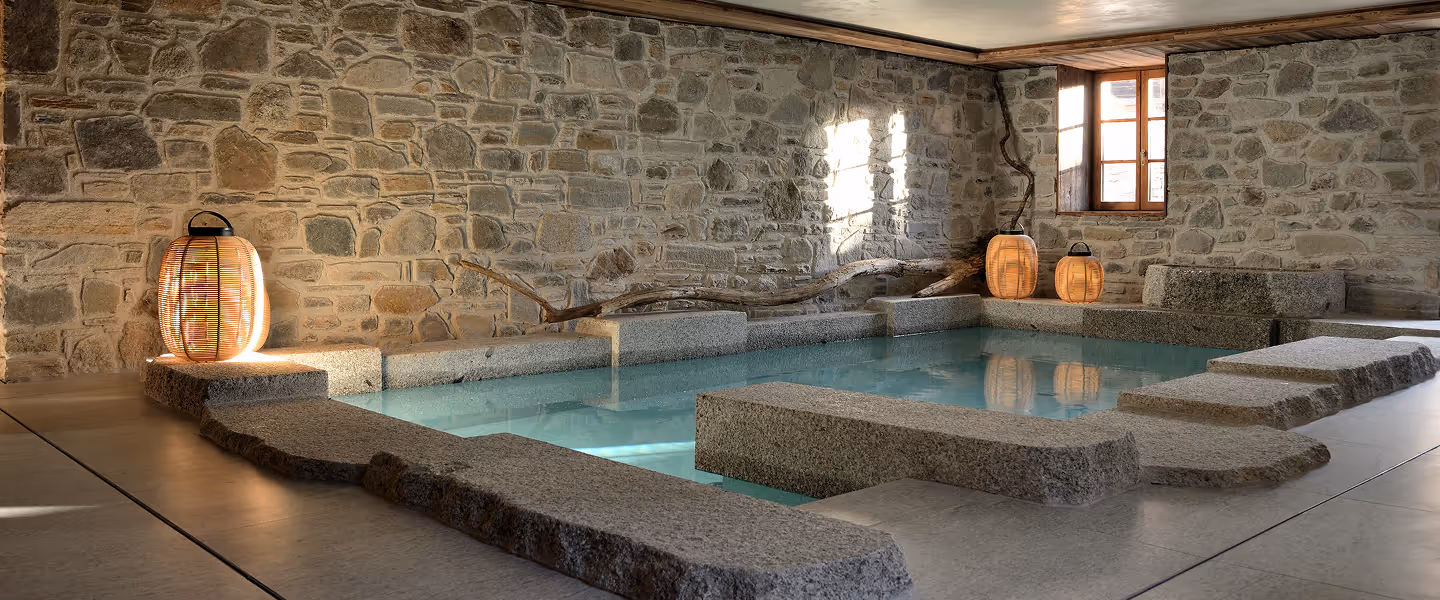 Piscine intérieure avec murs en pierre, structure en granite et lanternes en bois allumées, La Ferme des Drus, Chamonix-Mont-Blanc, France.